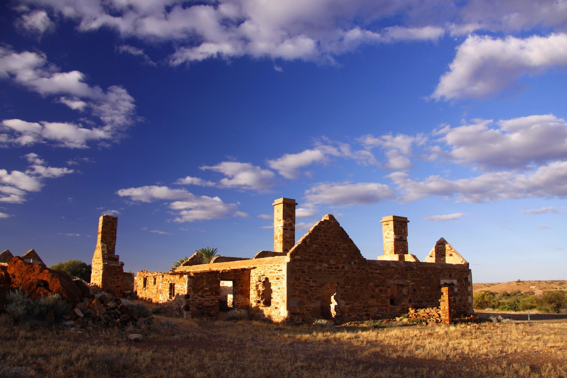 Abandoned buildings in the Australian Outback. The buildings are made of sandstone and are in various states of disrepair. The buildings are surrounded by desert landscape.