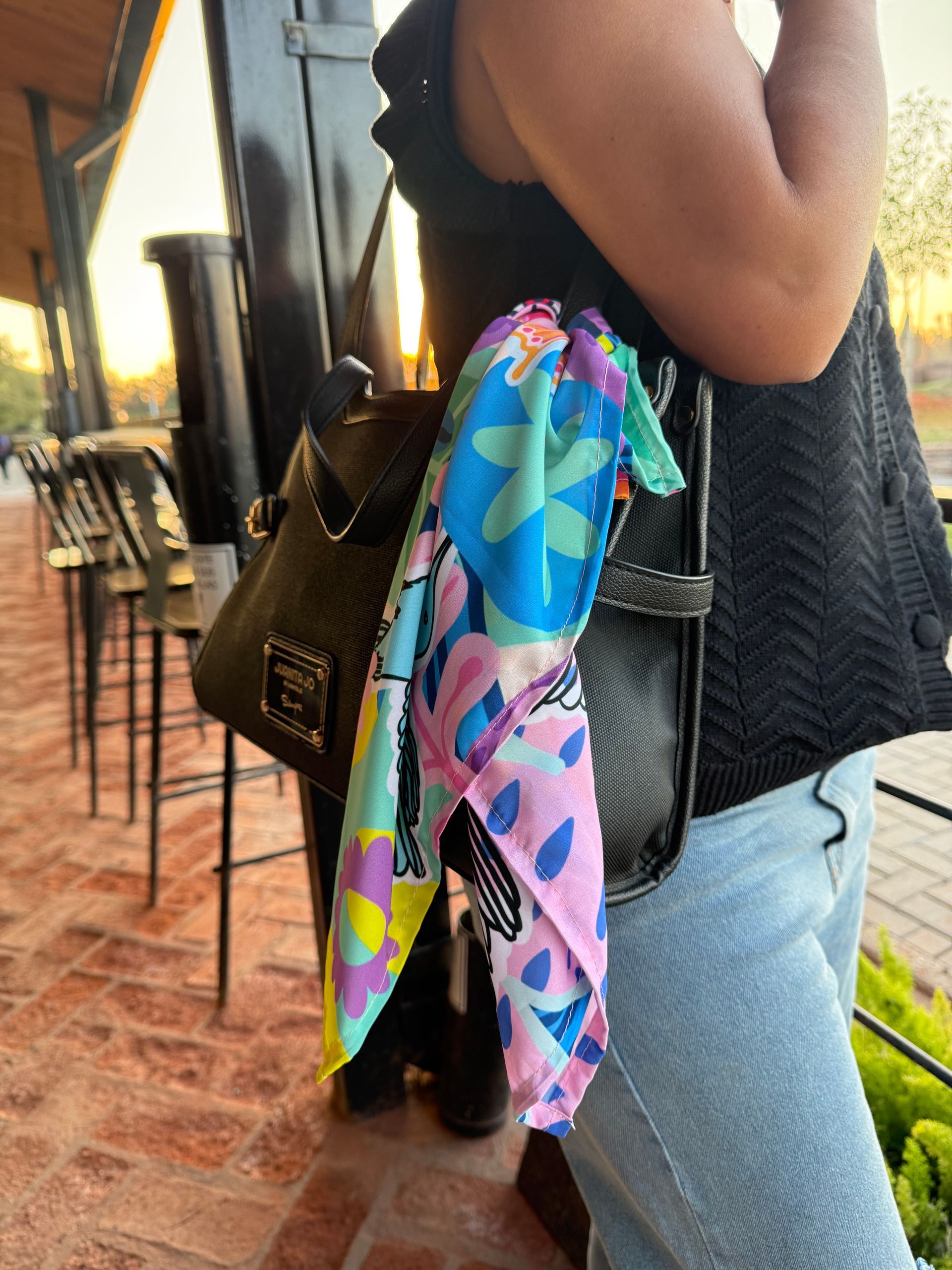 Mujer con bolso negro y bufanda colorida al aire libre.