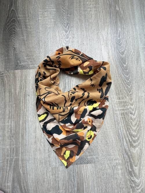 Bufanda infinita de color tostado y estampada sobre una superficie de madera gris.