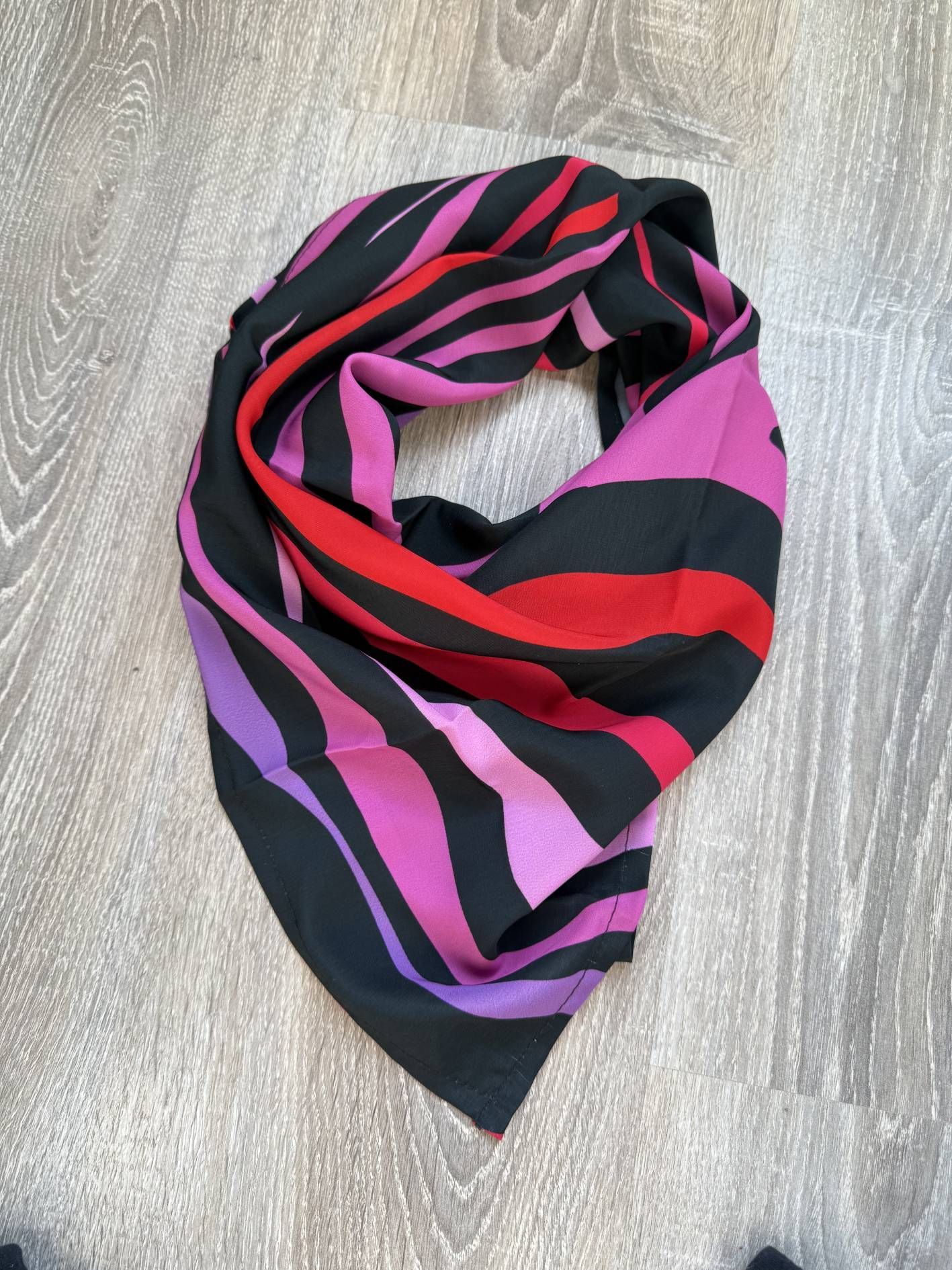 Bufanda circular con rayas de cebra negras, rojas y moradas, colocada sobre una superficie de madera.