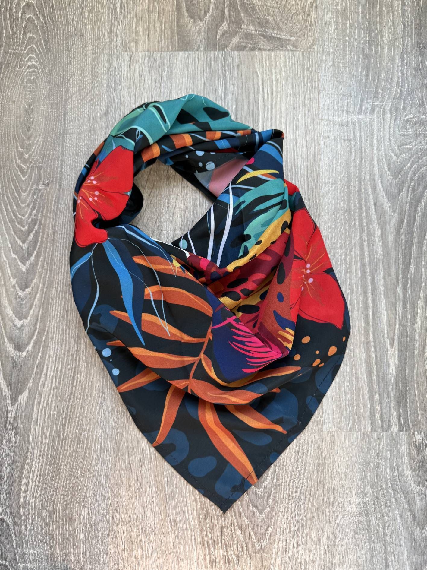 Bufanda infinita con estampado floral sobre una superficie de madera gris.