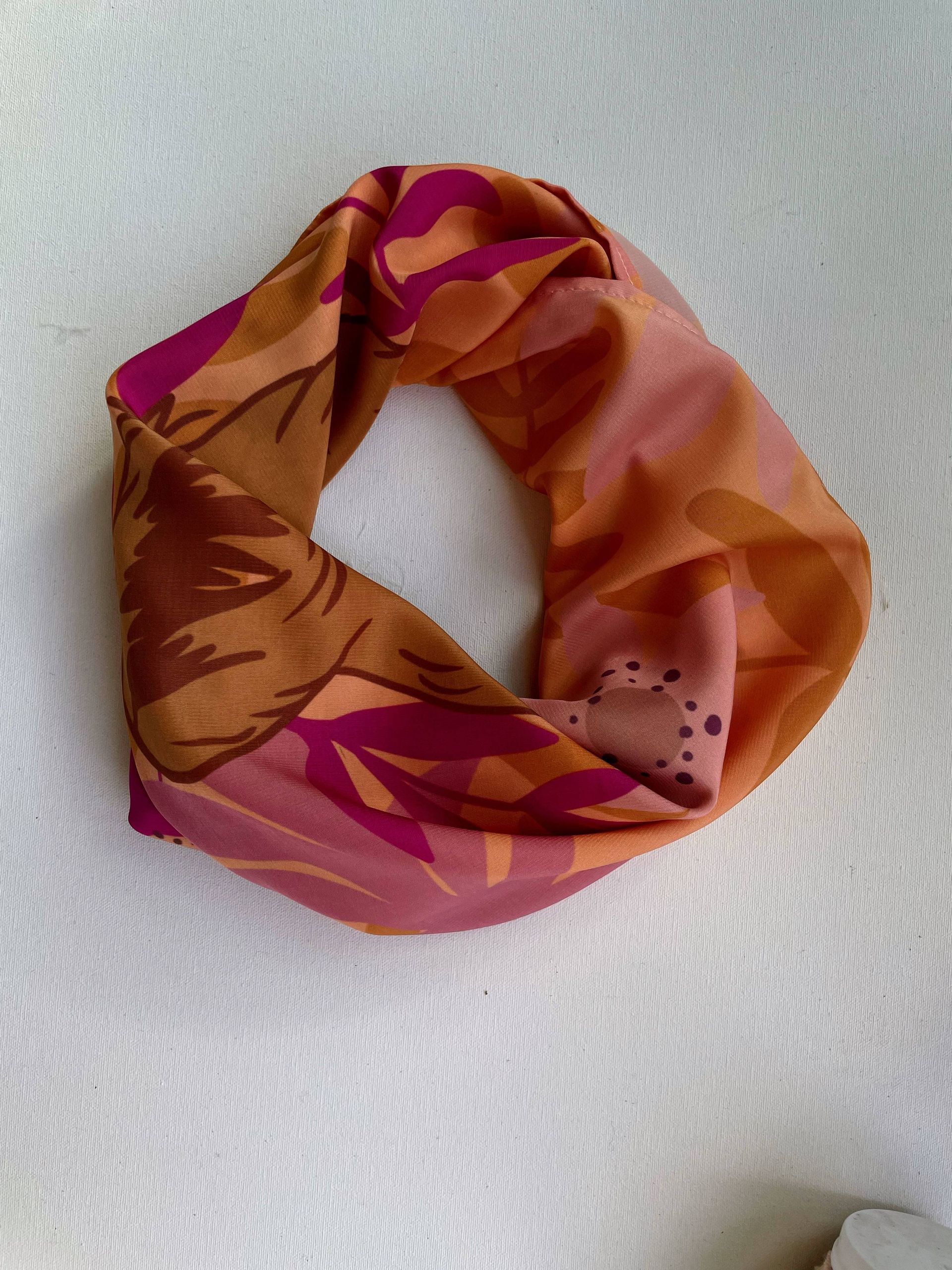 Bufanda circular con estampado floral en tonos naranja, rosa y marrón, colocada sobre tela blanca.