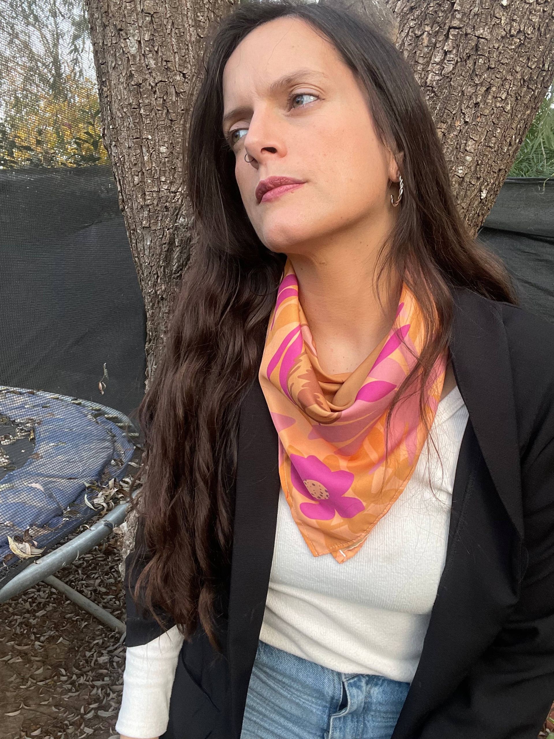 Una mujer que lleva una bufanda alrededor del cuello está parada frente a un árbol.