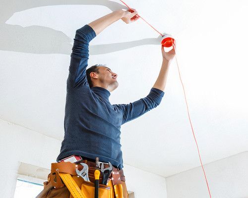 Un homme mesure un plafond avec un ruban à mesurer.