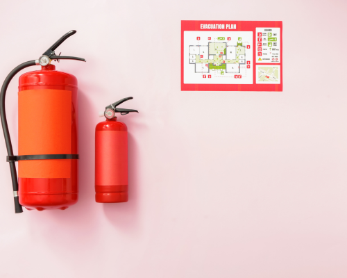 Deux extincteurs rouges sont accrochés sur un mur rose à côté d'un plan d'évacuation.