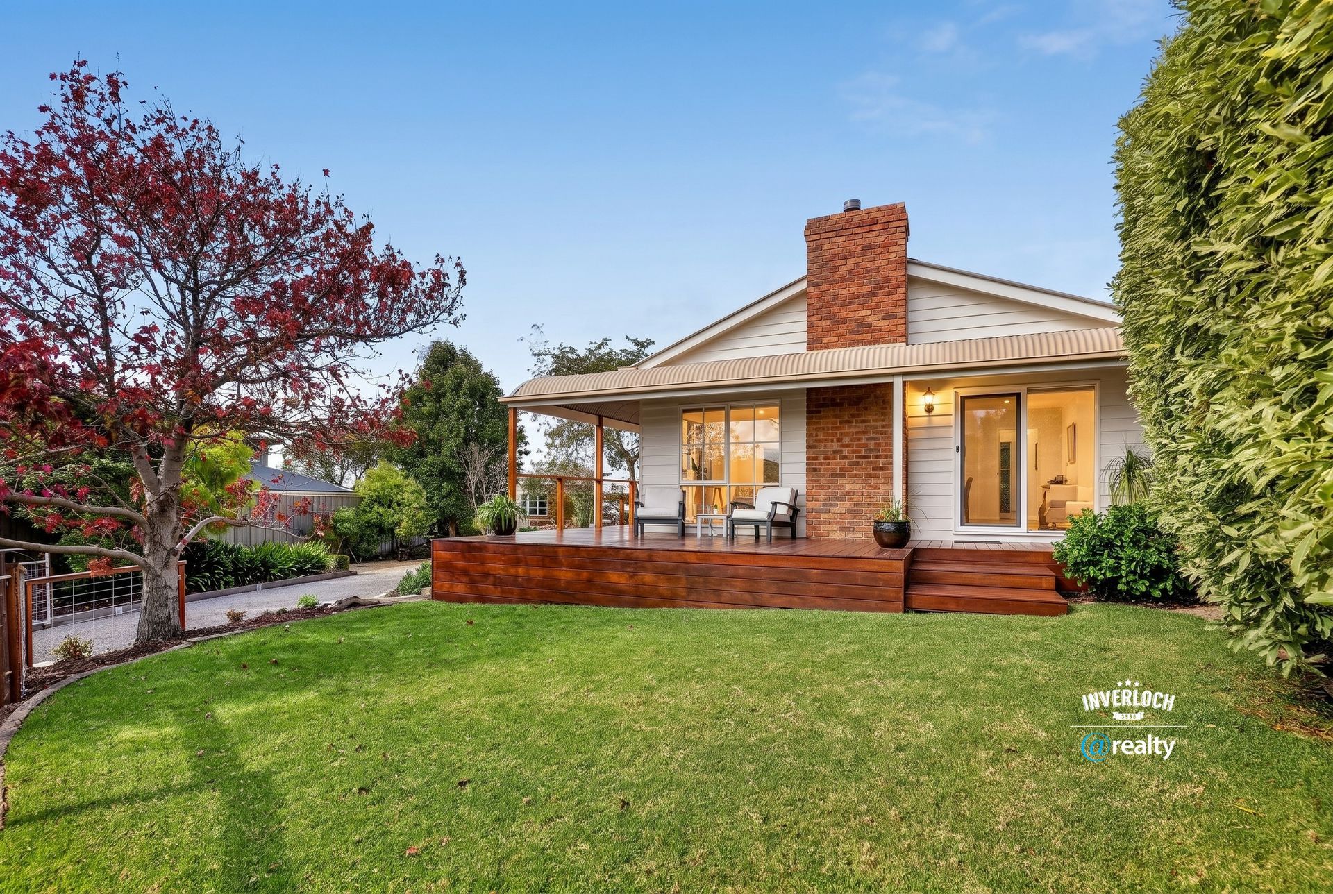 Brick house with a front porch, large green lawn, and trees at sunset