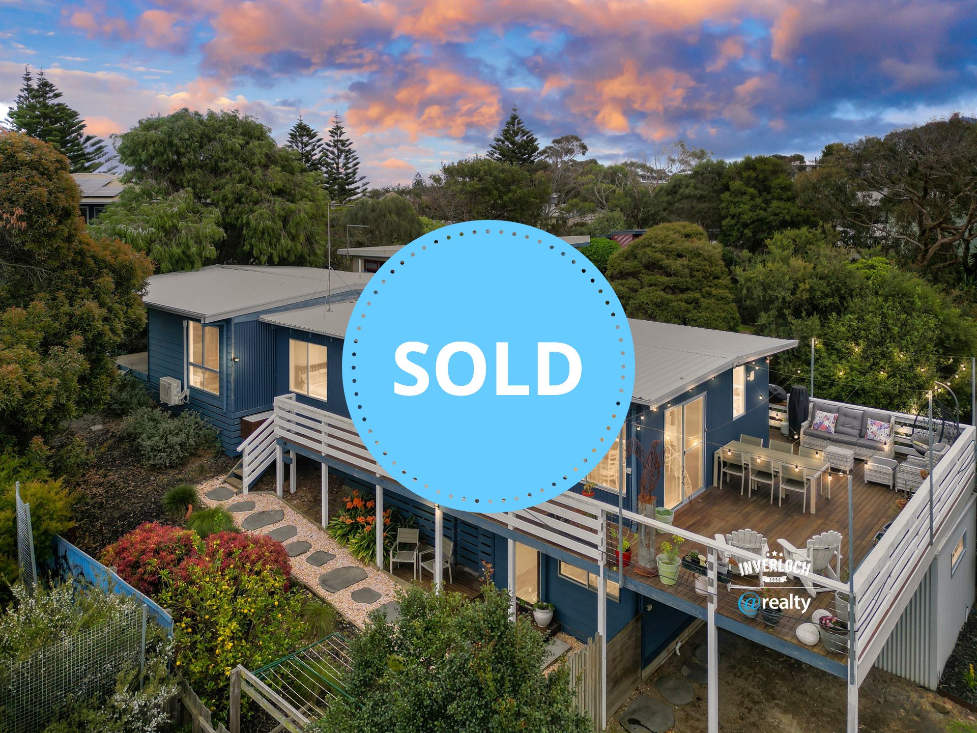 An aerial view of a blue house with a large deck surrounded by trees.