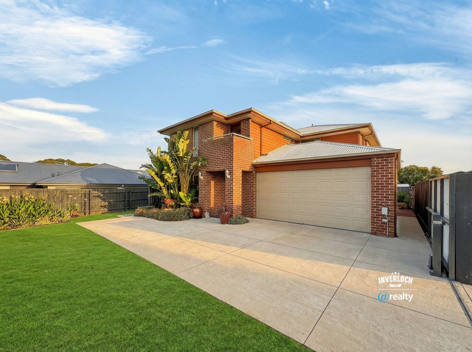 Suburban brick house with a double garage, driveway, and neatly kept lawn under a blue sky