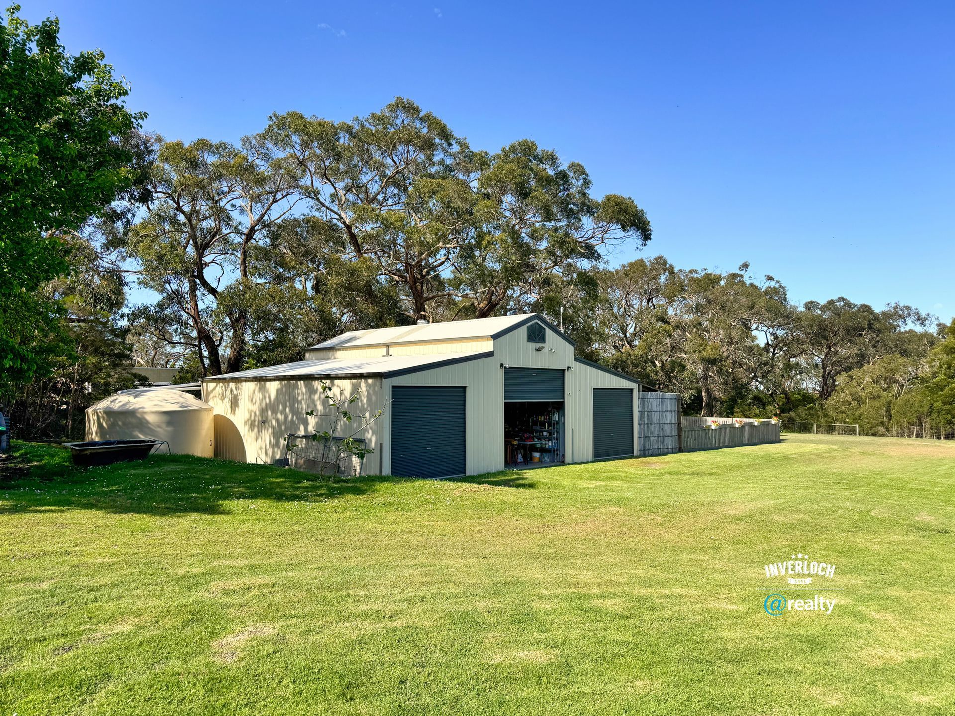 A white barn with three garage doors and a trailer on a grassy lawn; trees in the background.