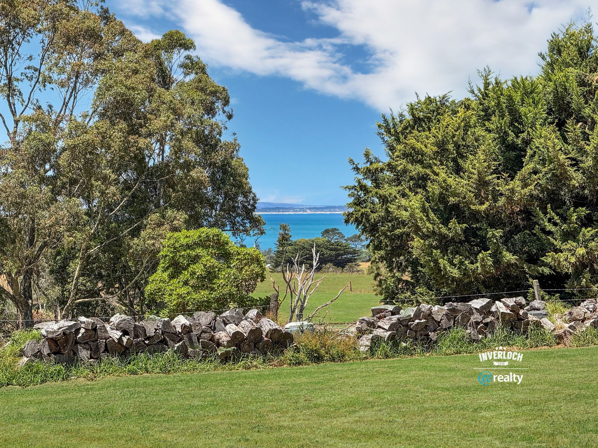 Green lawn with stone wall framing a view of blue ocean and sky, trees on each side.