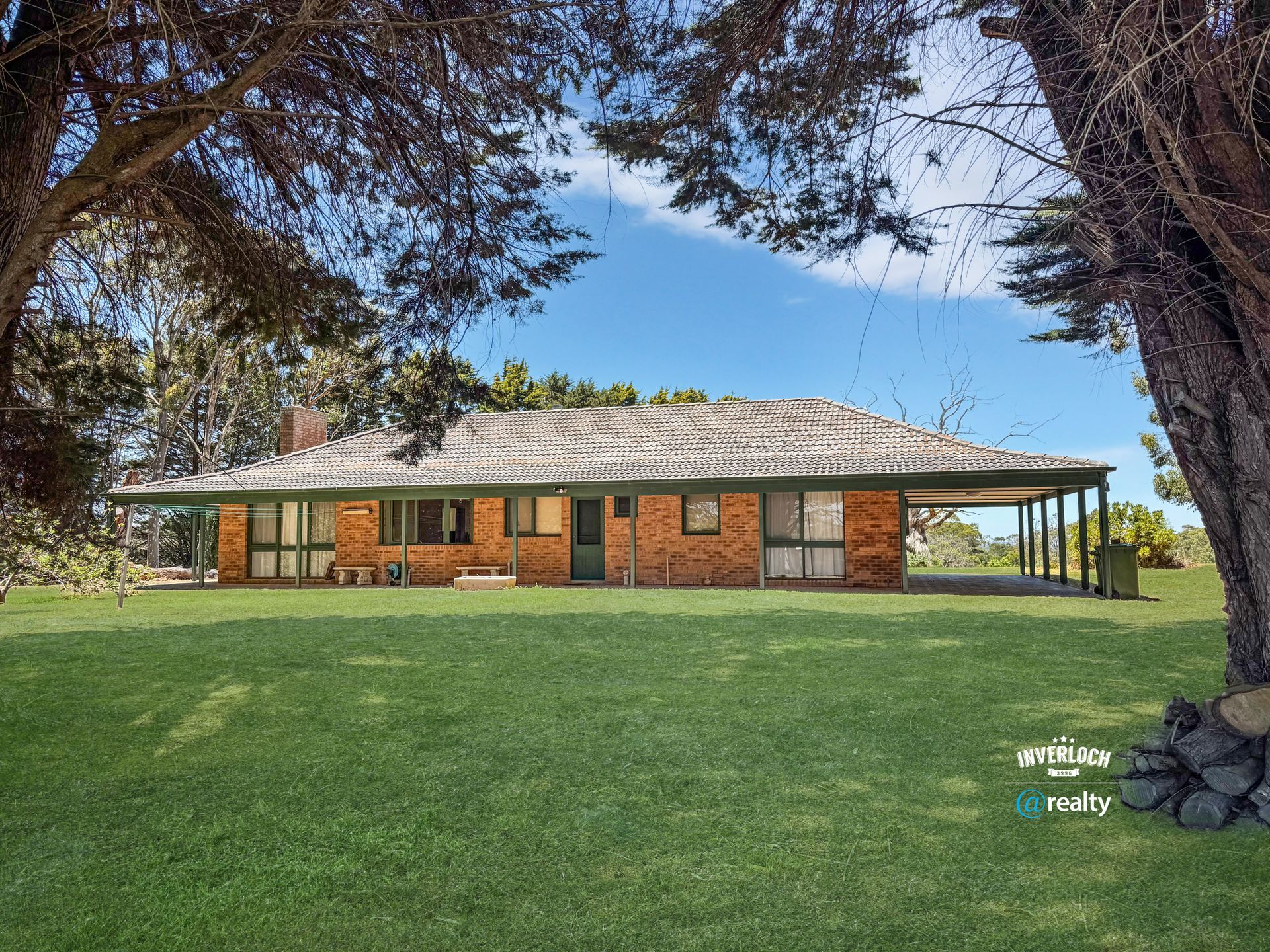 Brick house with a covered porch on a grassy lawn under a blue sky, framed by trees.