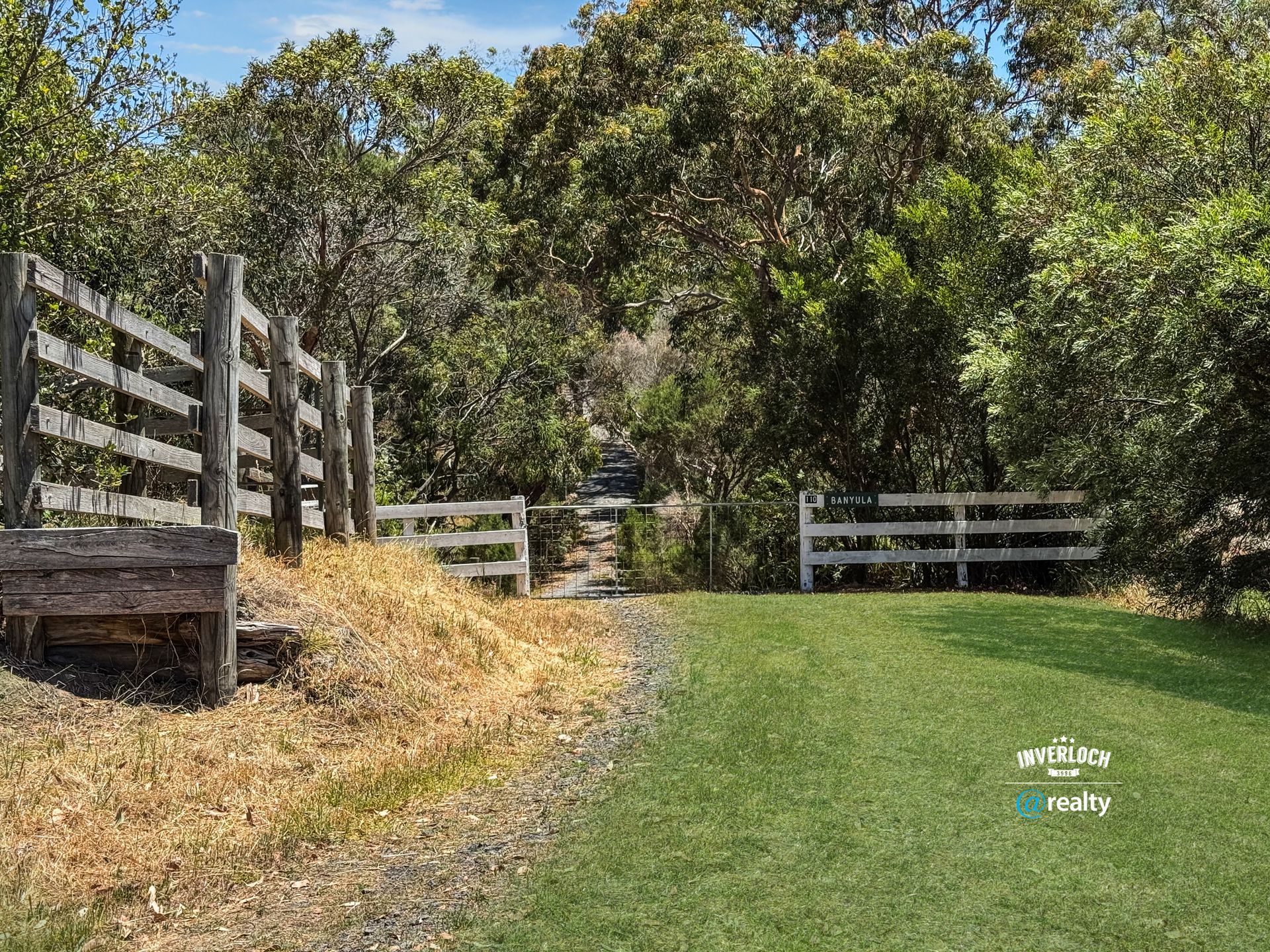 A wooden fence surrounds a grassy field with trees in the background.
