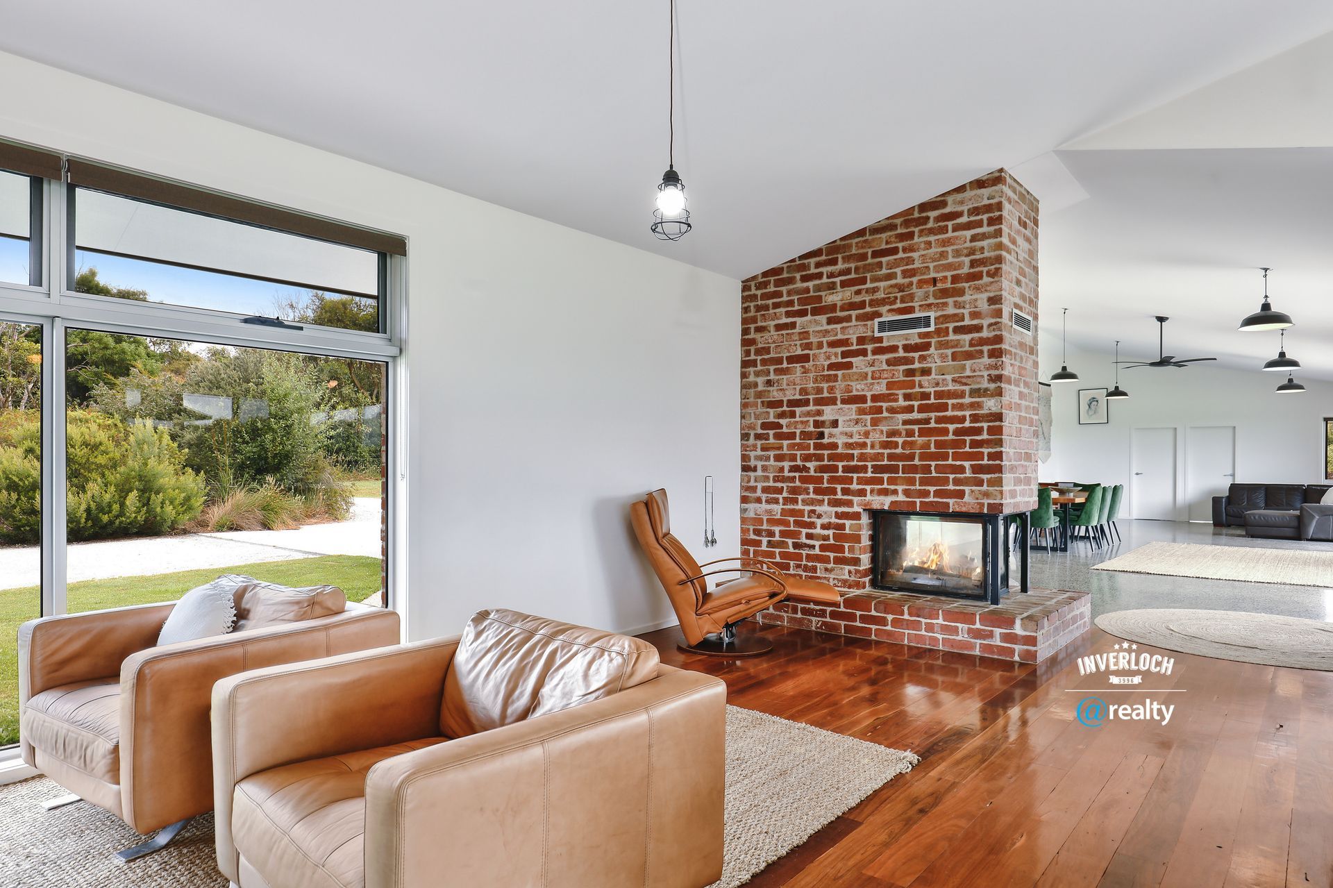 Living room with brick fireplace, leather chairs, and large window overlooking greenery.