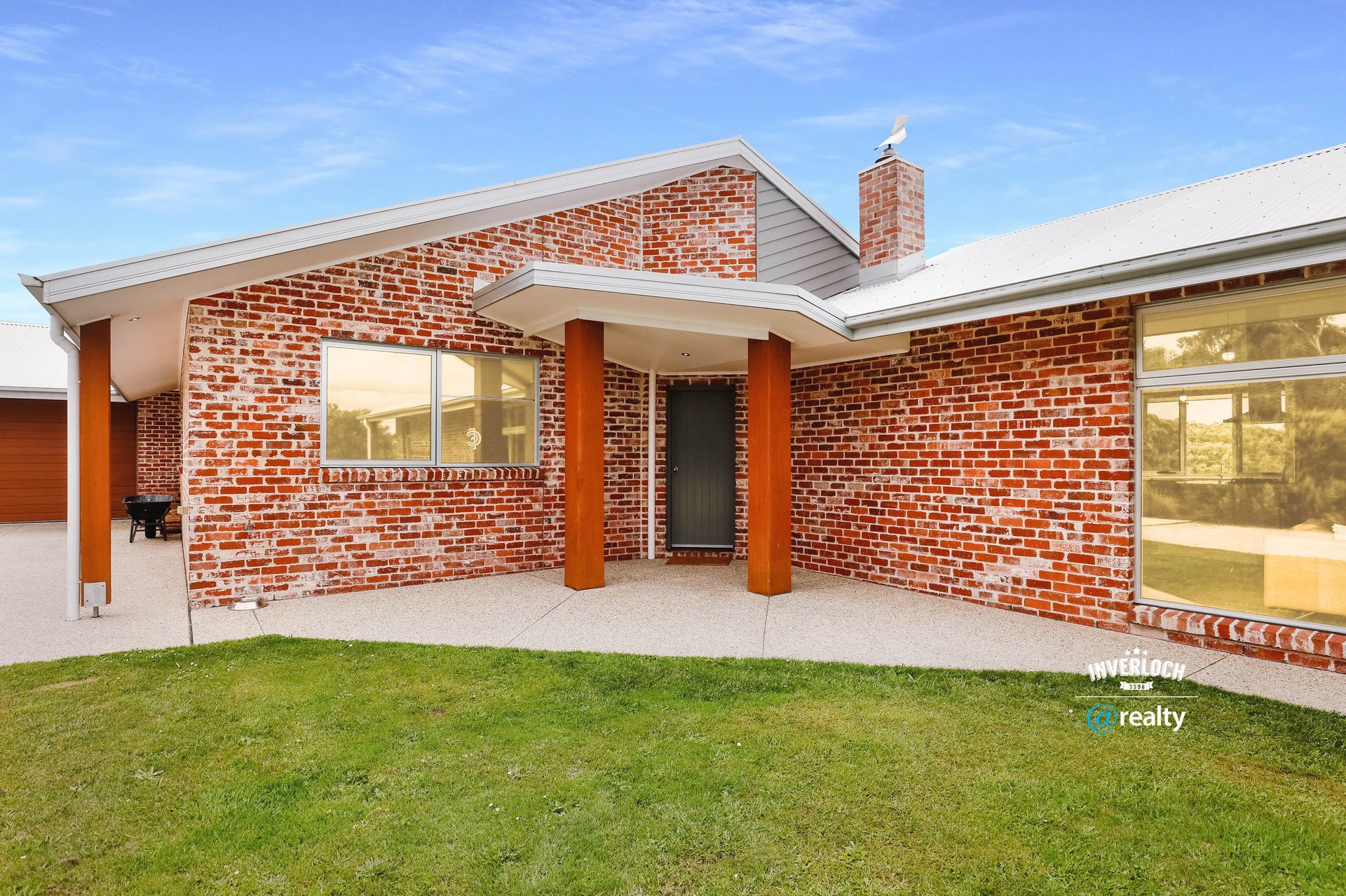 Red brick house with a green lawn under a blue sky.