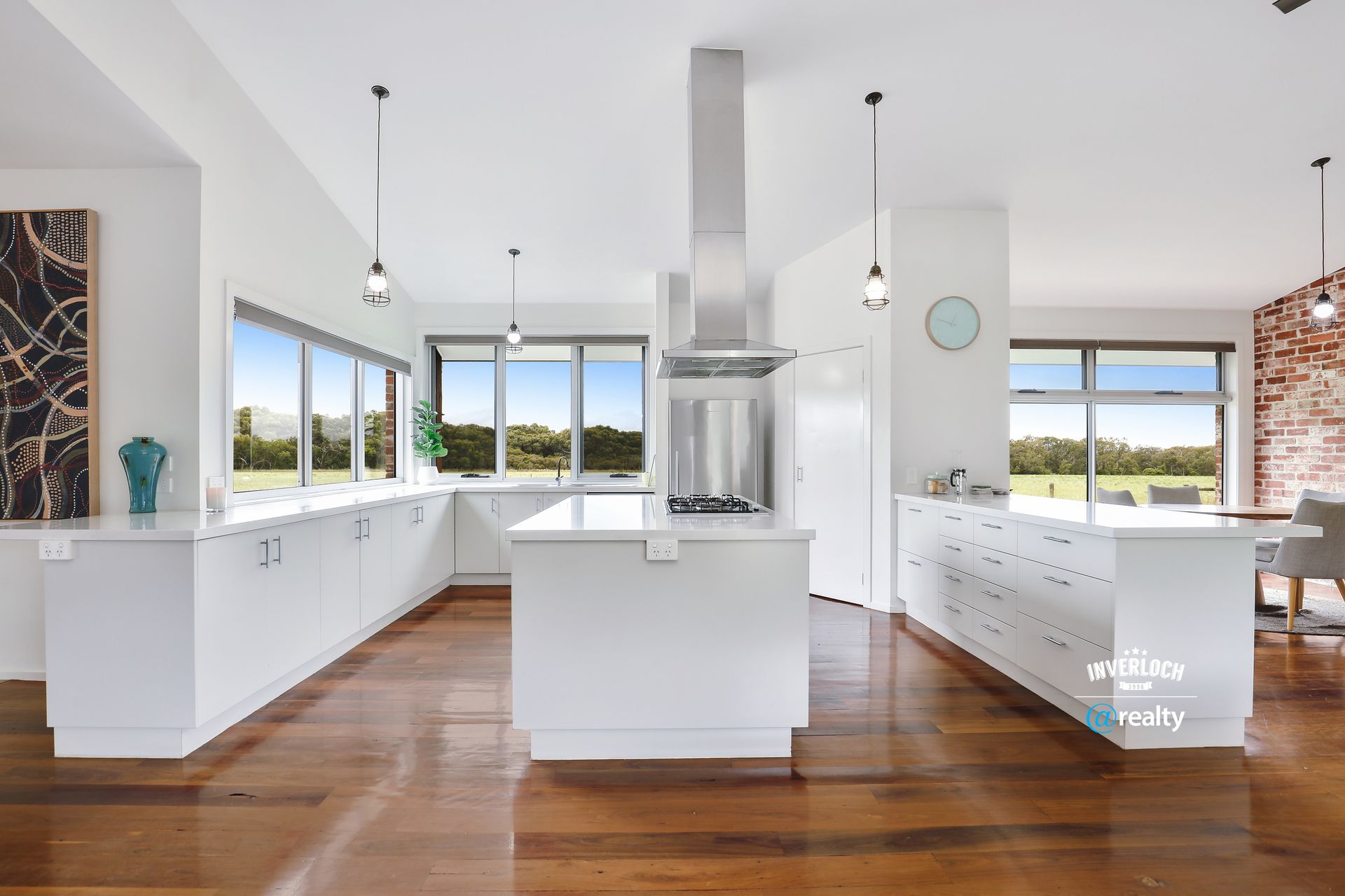 Bright, modern kitchen with white cabinetry, wooden floors, stainless steel range hood, and large windows.