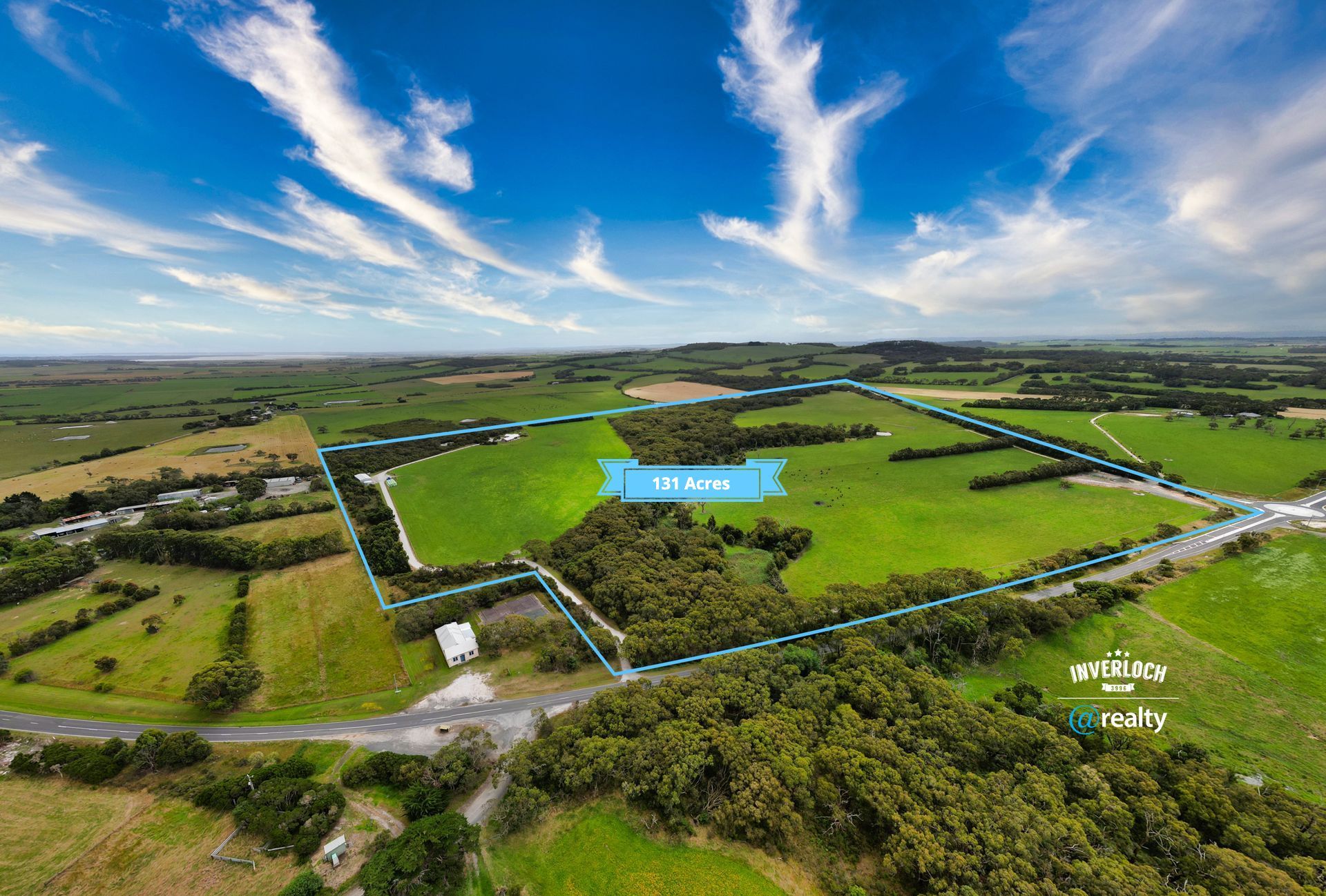 An aerial view of a large green field with trees and a road.