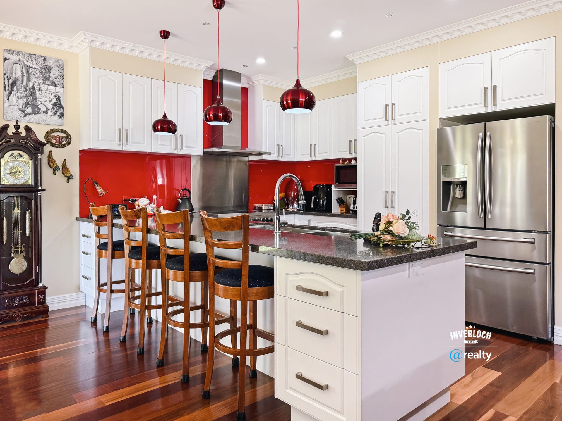 Bright kitchen with white cabinets, red backsplash, island with stools, and stainless steel appliances.