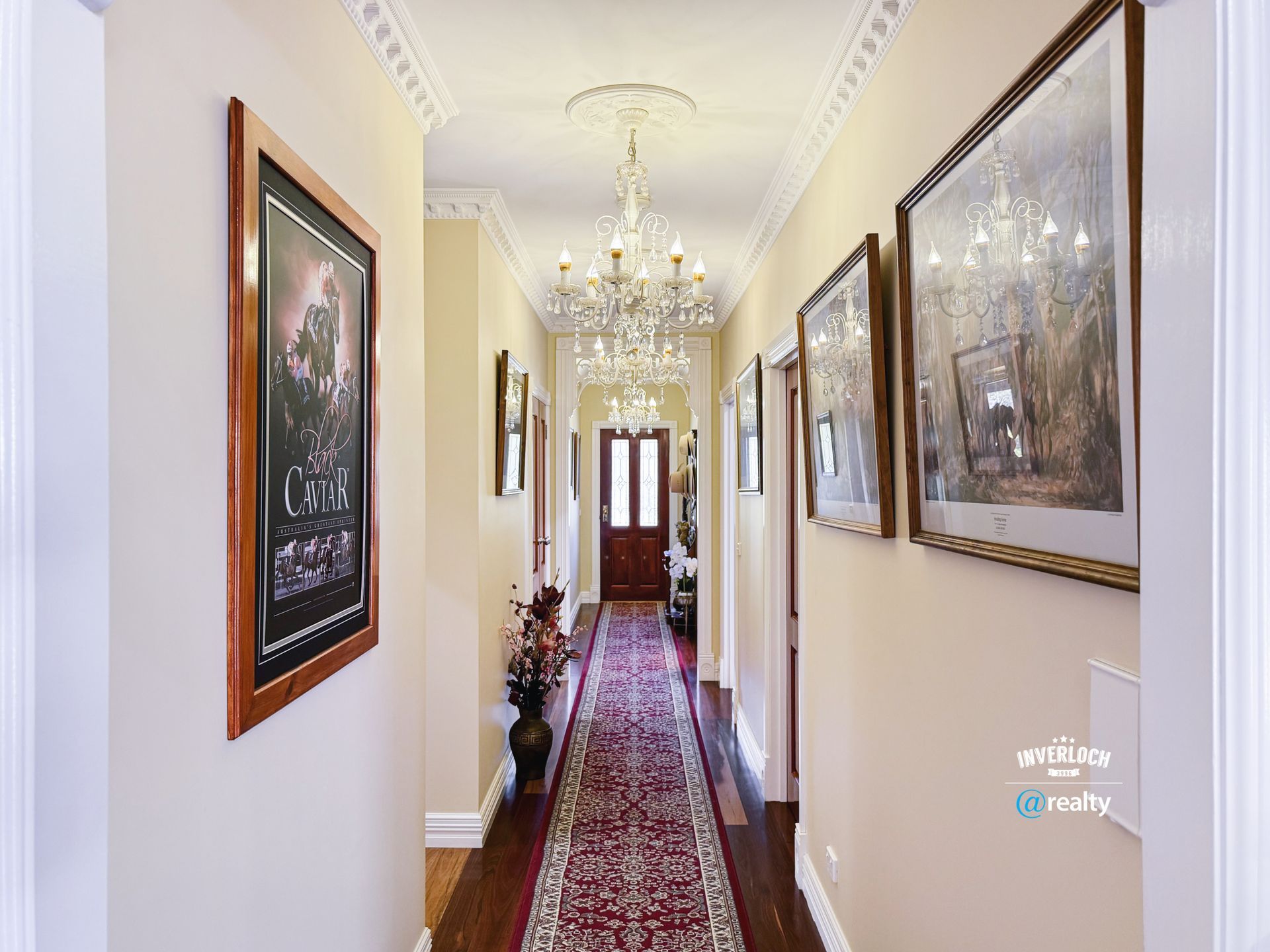 Hallway with ornate crown molding, chandelier, framed artwork, and red runner rug.