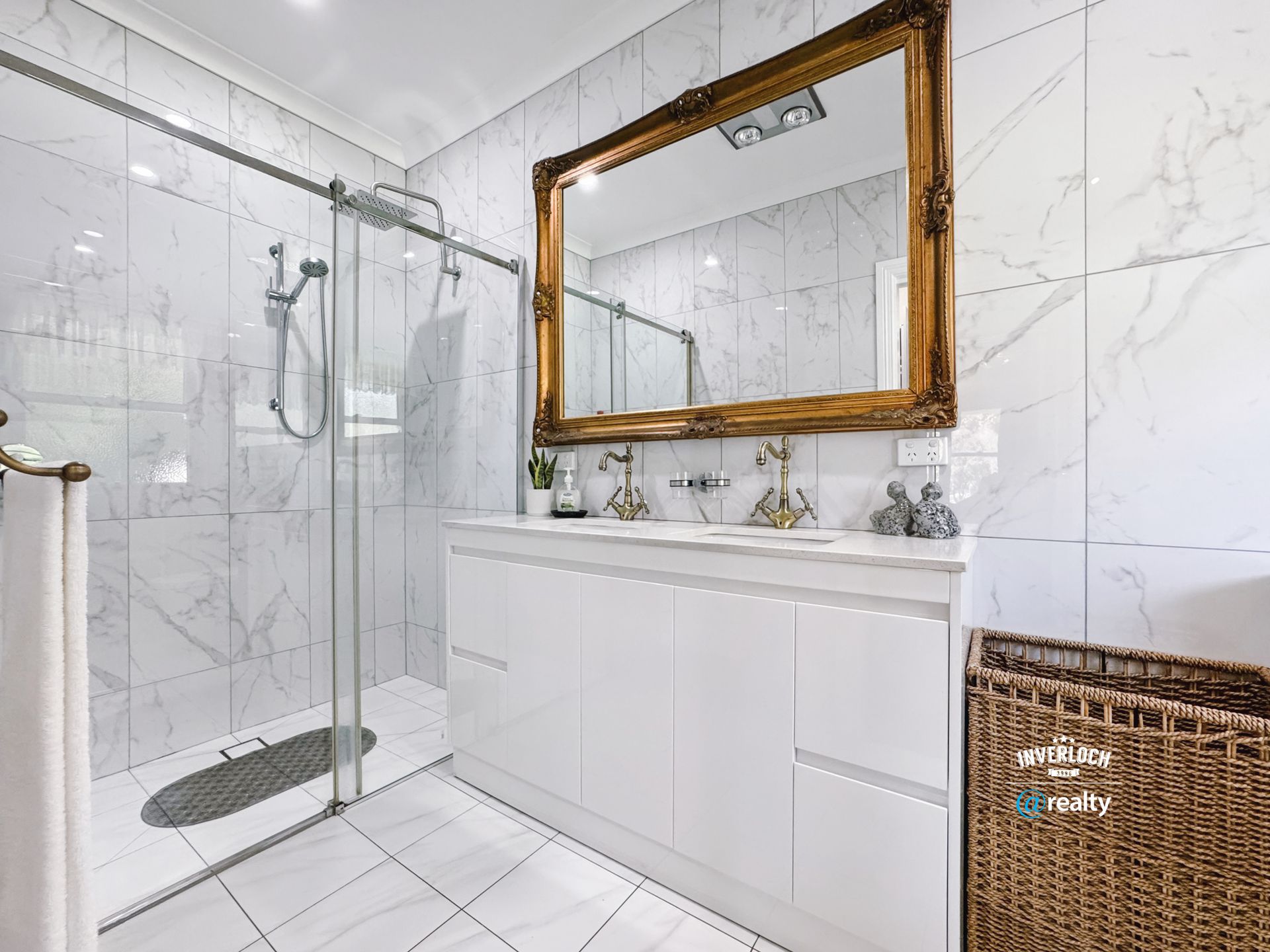 Bathroom with marble tiles, a glass shower, large gold-framed mirror, and white vanity.