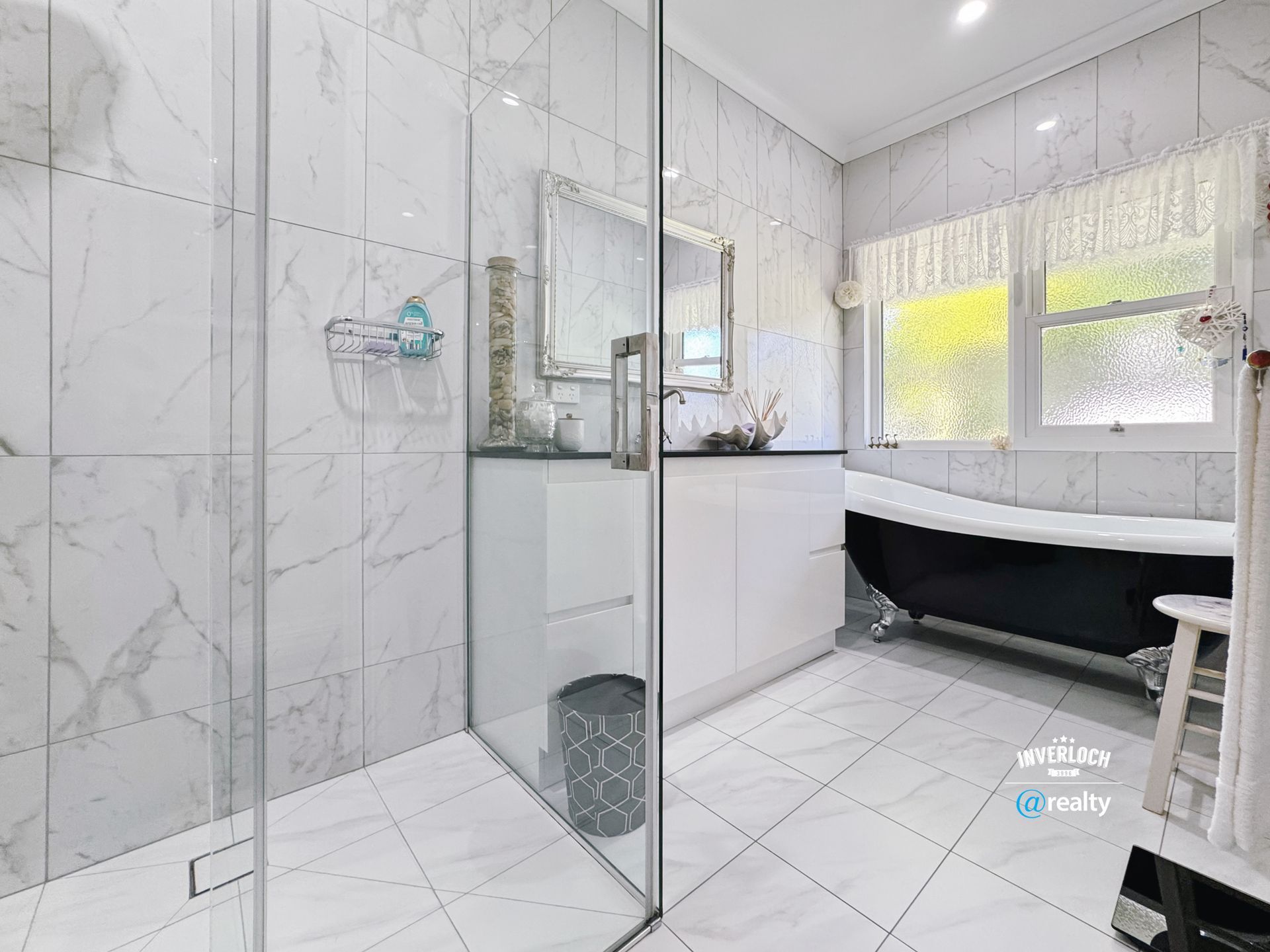 White marble tiled bathroom with shower, black bathtub, and white cabinets.