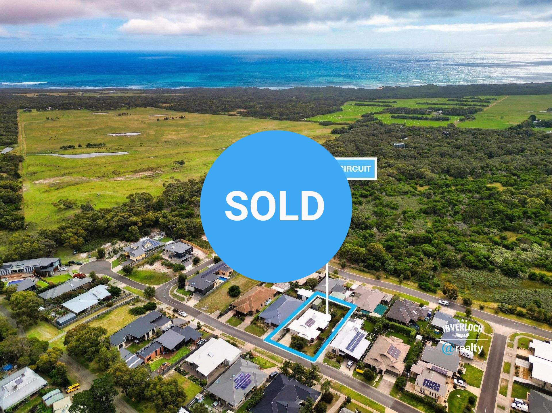 Aerial view of a residential neighborhood near the ocean, with a specific house highlighted in blue.