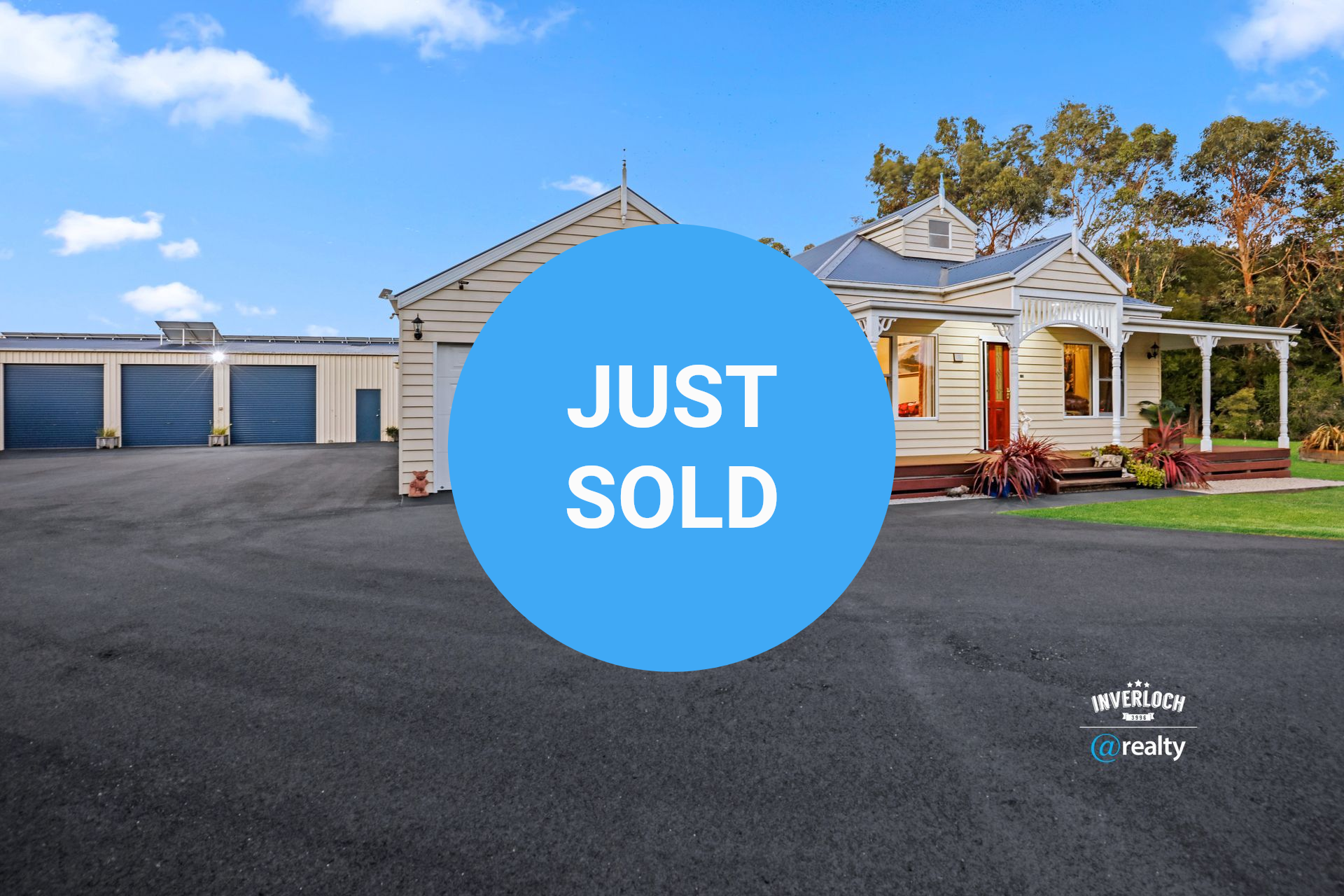 Victorian style house with detached garage and storage units on a paved driveway; bright blue sky.