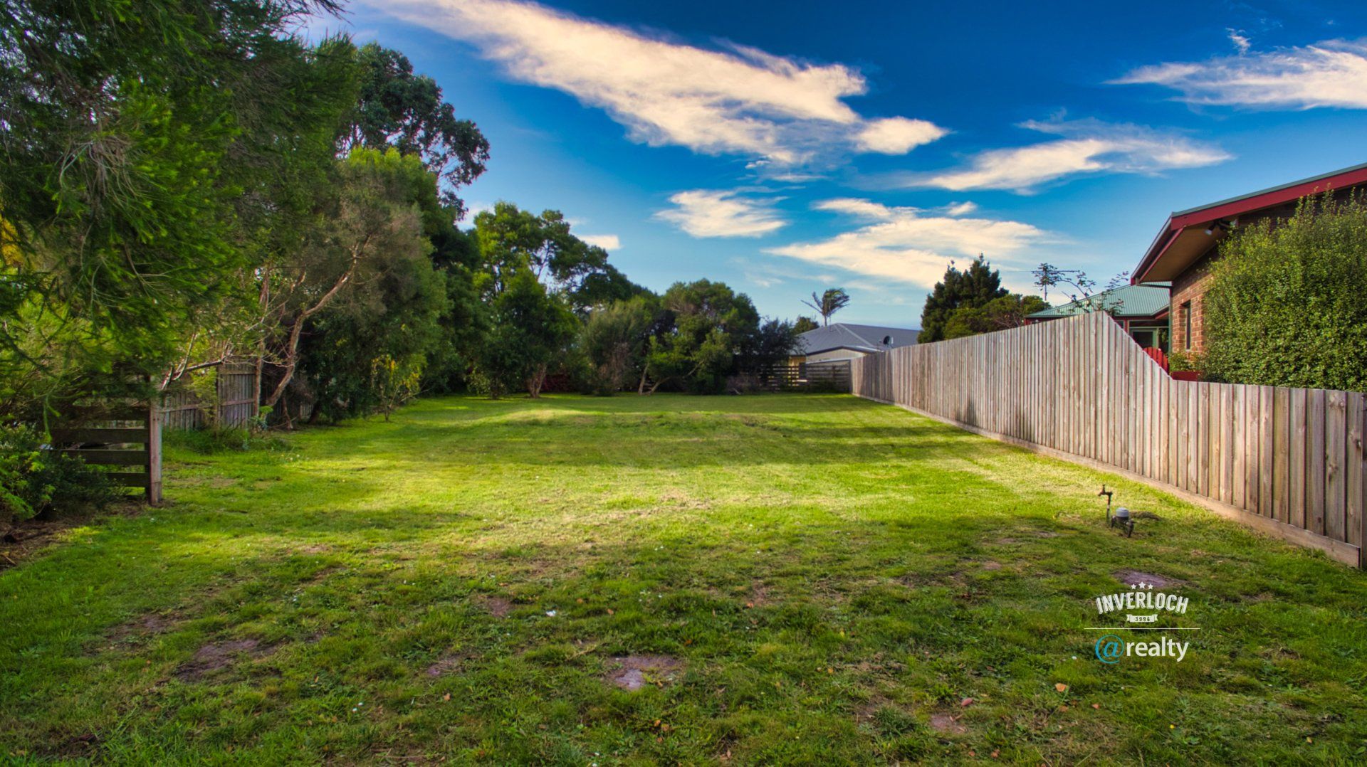 An empty yard with a wooden fence and a house in the background.