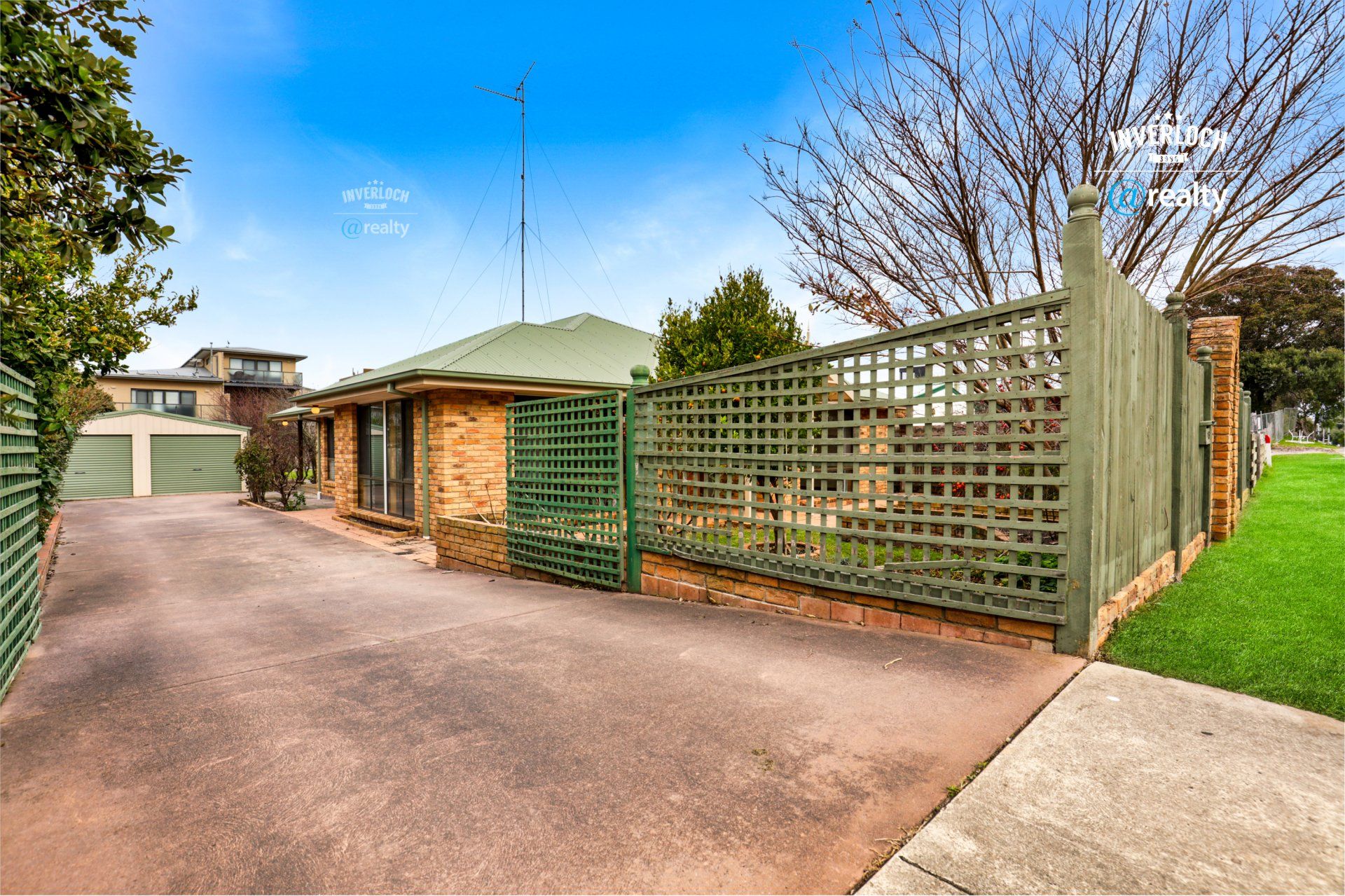 A house with a green fence and a driveway leading to it.