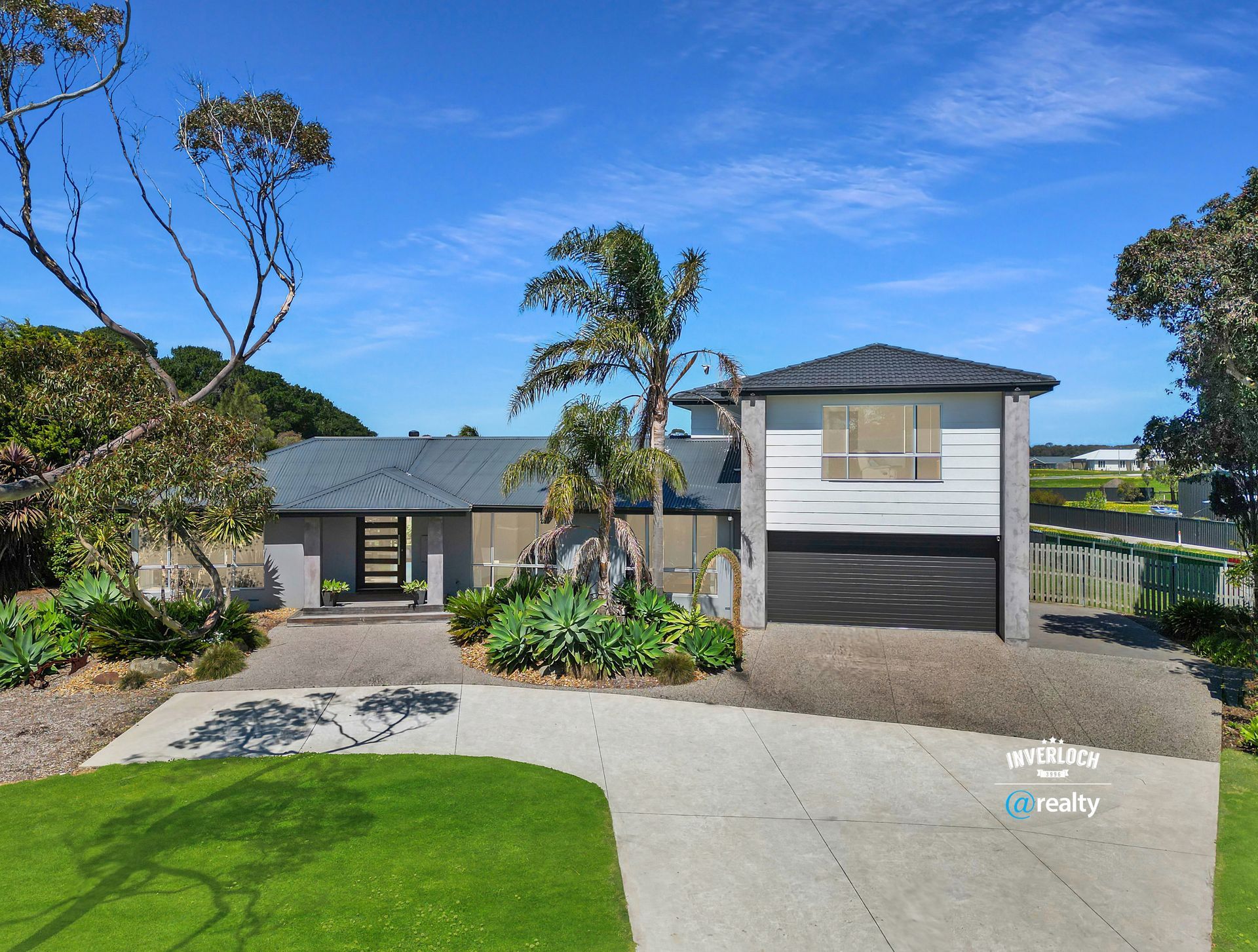 Modern gray home with driveway and detached garage under a clear blue sky.