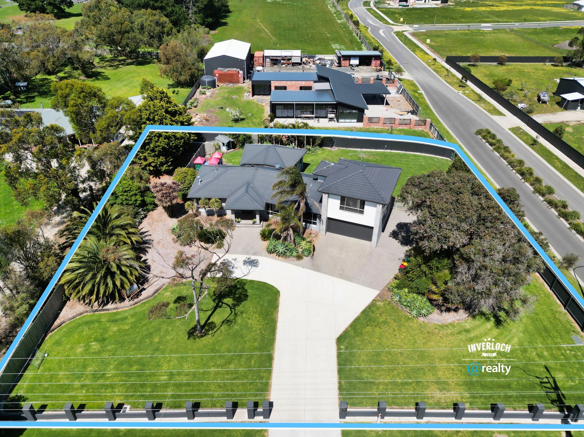 Aerial view of a house with a driveway and surrounding lawn, outlined in blue. Other houses and a street are visible.