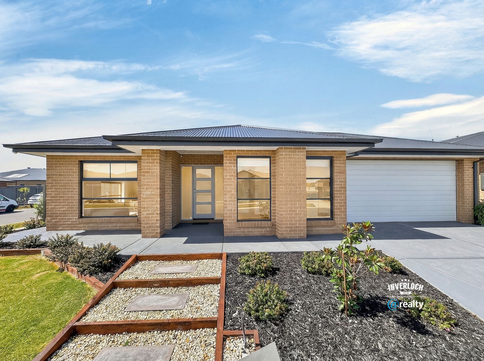 Single-story brick house with a gray roof and garage, manicured front yard, and walkway on a sunny day.
