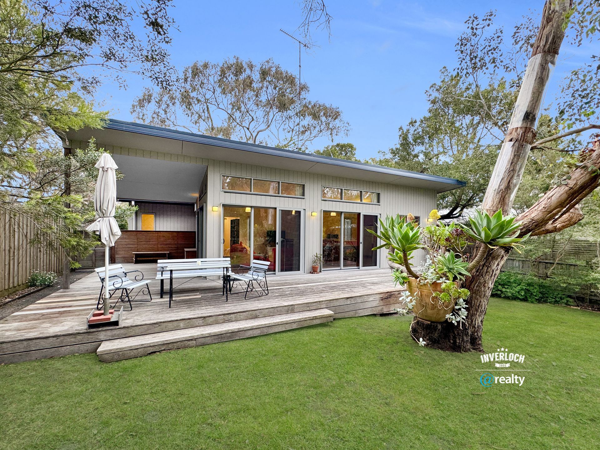 A modern house with a deck and lawn, surrounded by trees.