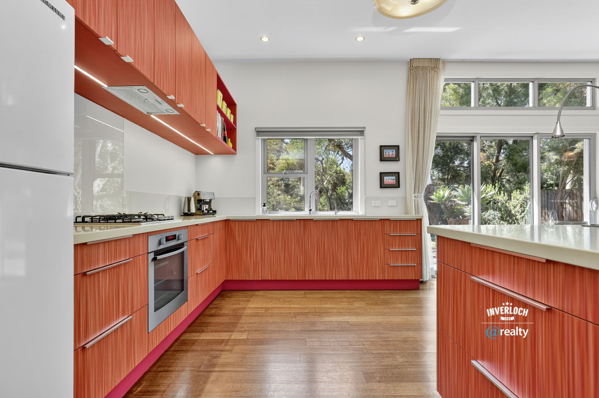 Modern kitchen with red cabinetry, white countertops, stainless steel appliances, and wooden floors.