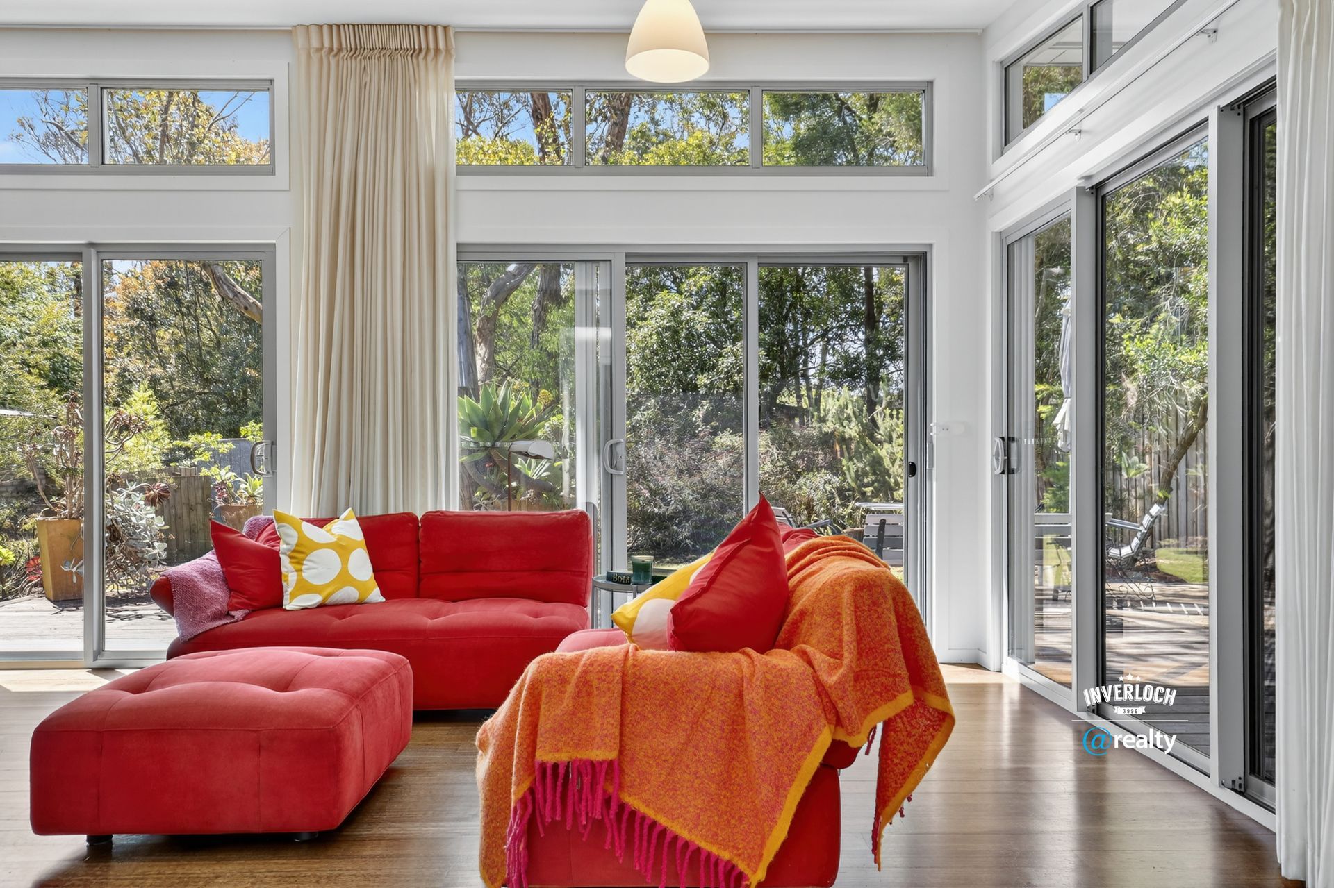 Living room with red sofa, ottoman, and orange throw blanket near sliding glass doors overlooking greenery.