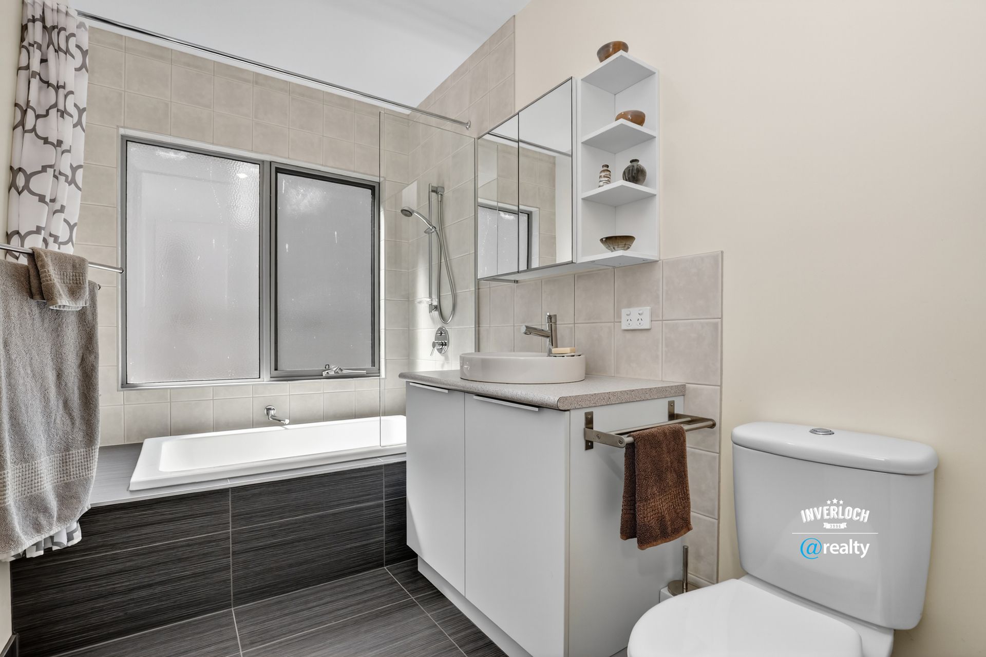 Modern bathroom with a bathtub, toilet, sink, and mirrored cabinet. Beige and black tiles.