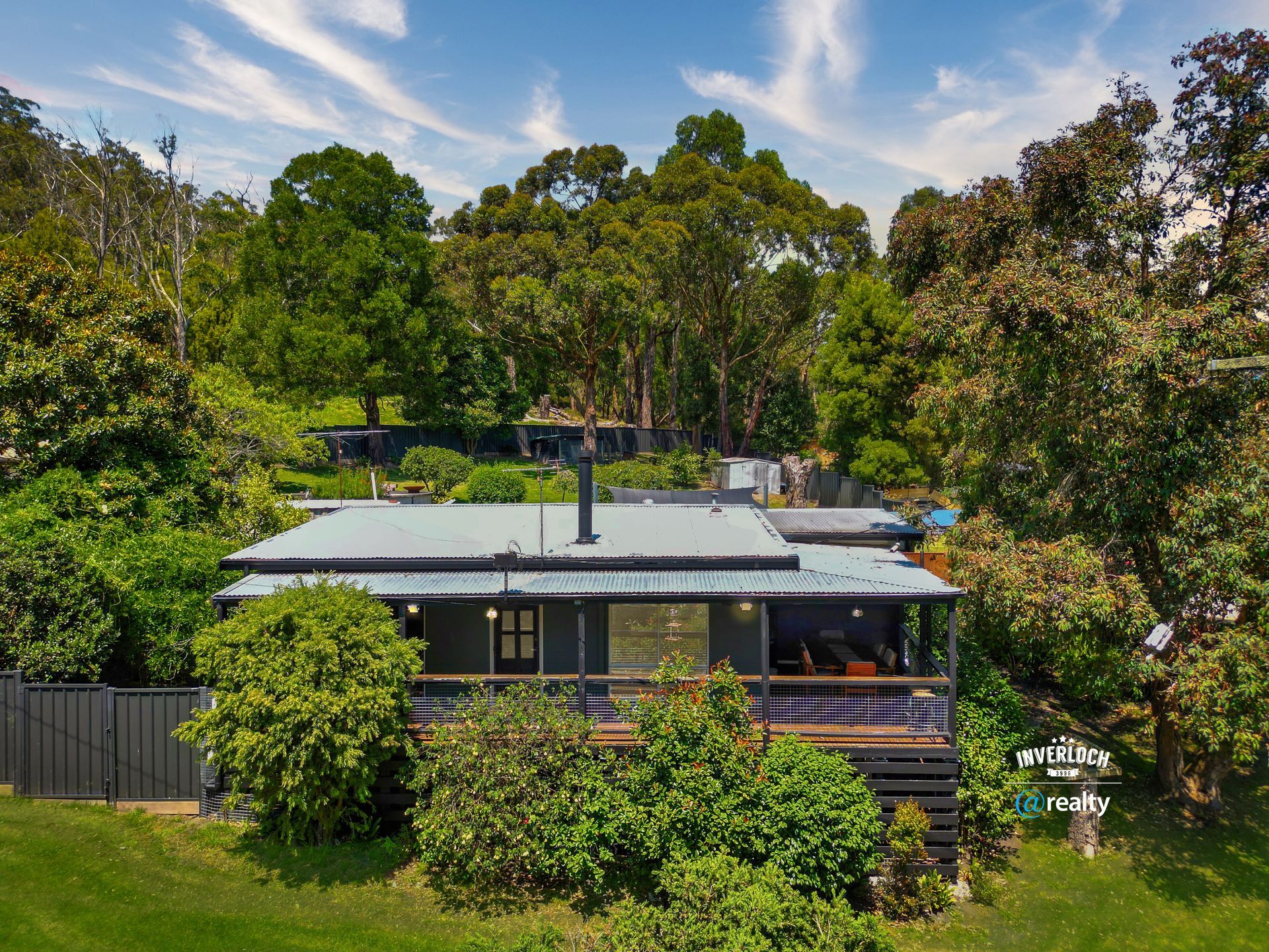 House nestled amongst lush greenery on a sunny day, with a dark roof and porch.