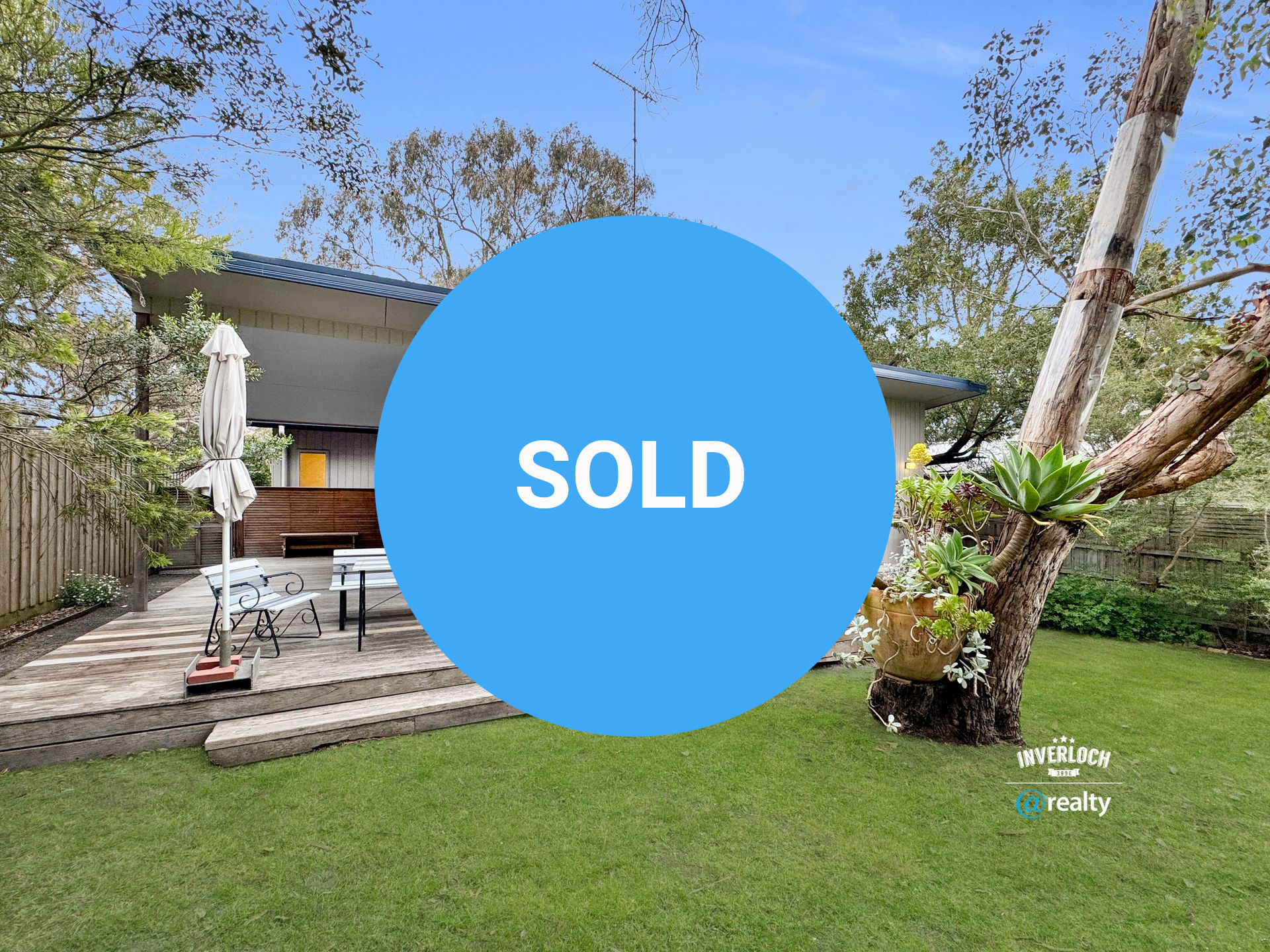 Modern home with deck and lawn, surrounded by trees.