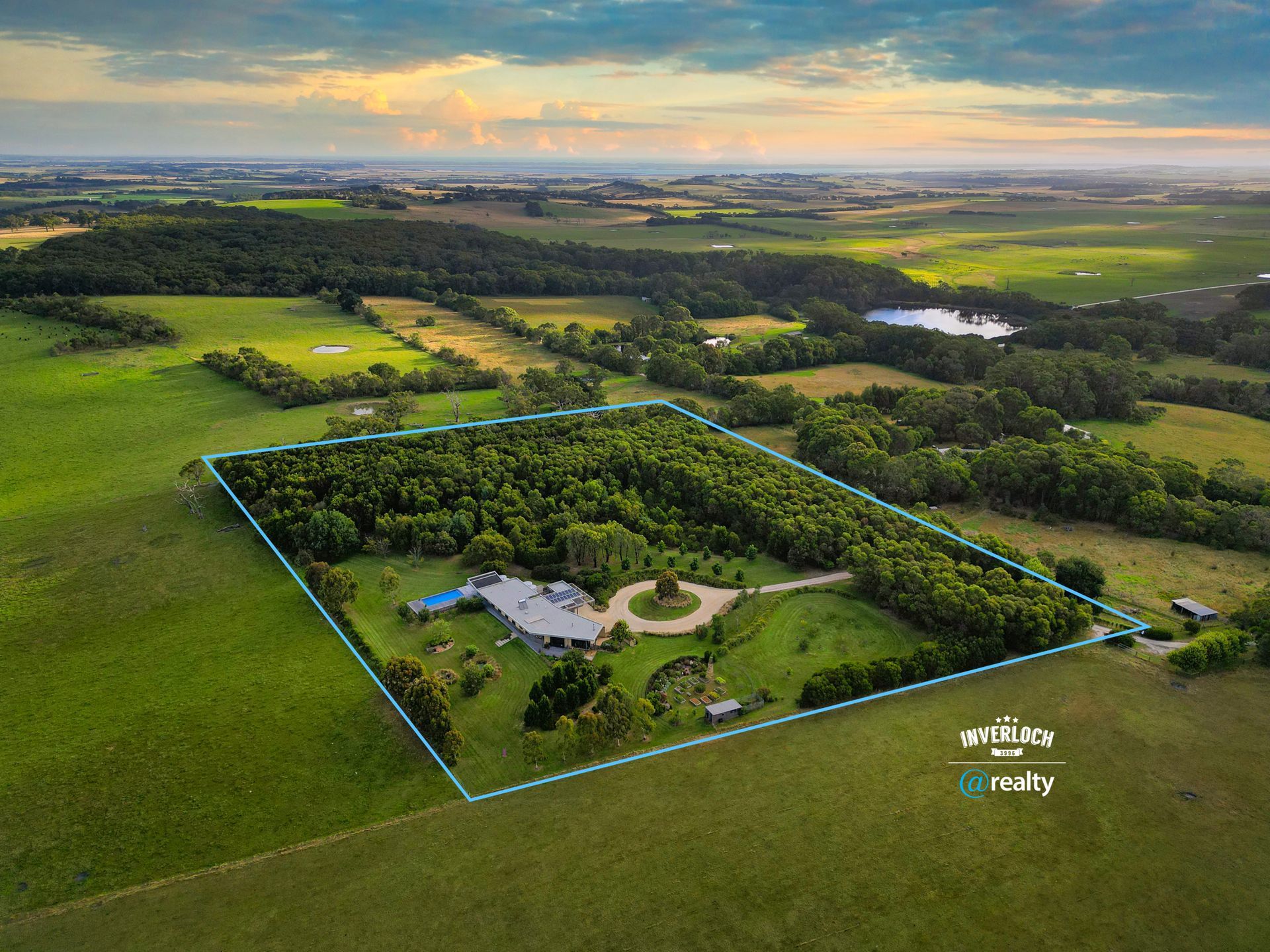 An aerial view of a large lush green field with a house in the middle.