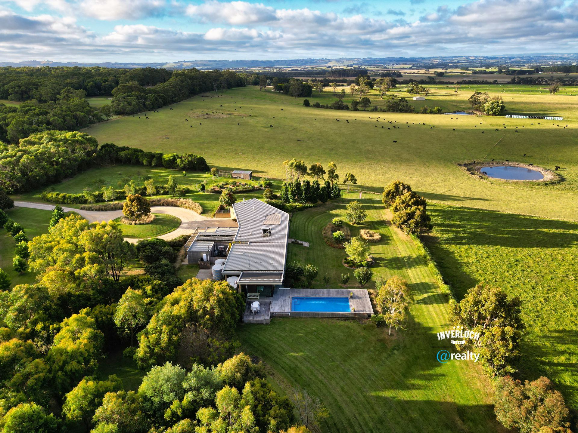 an aerial view of a house with a pool in the middle of a field surrounded by trees .