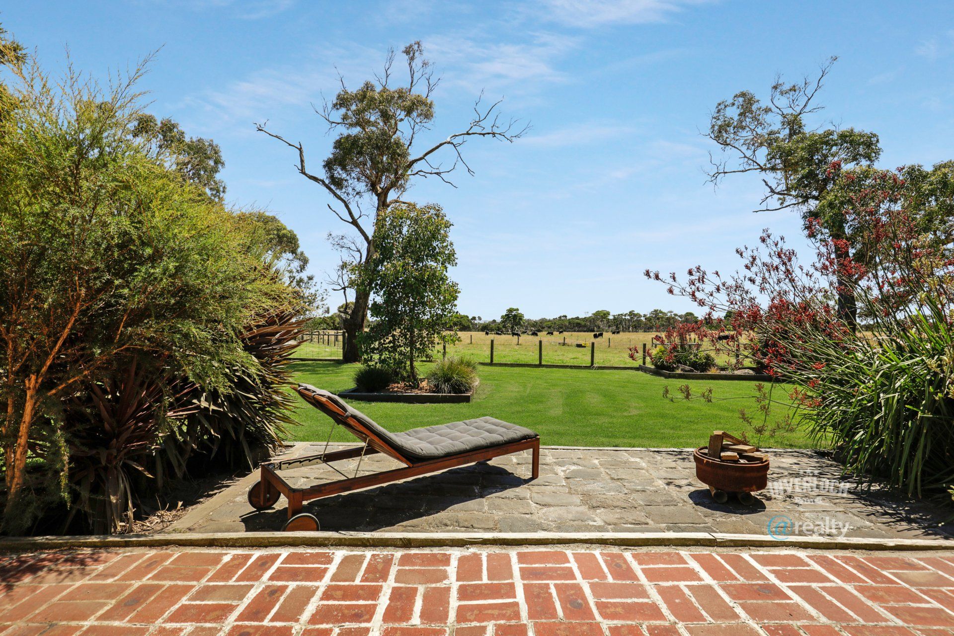 A lawn chair is sitting on a brick patio overlooking a lush green field.