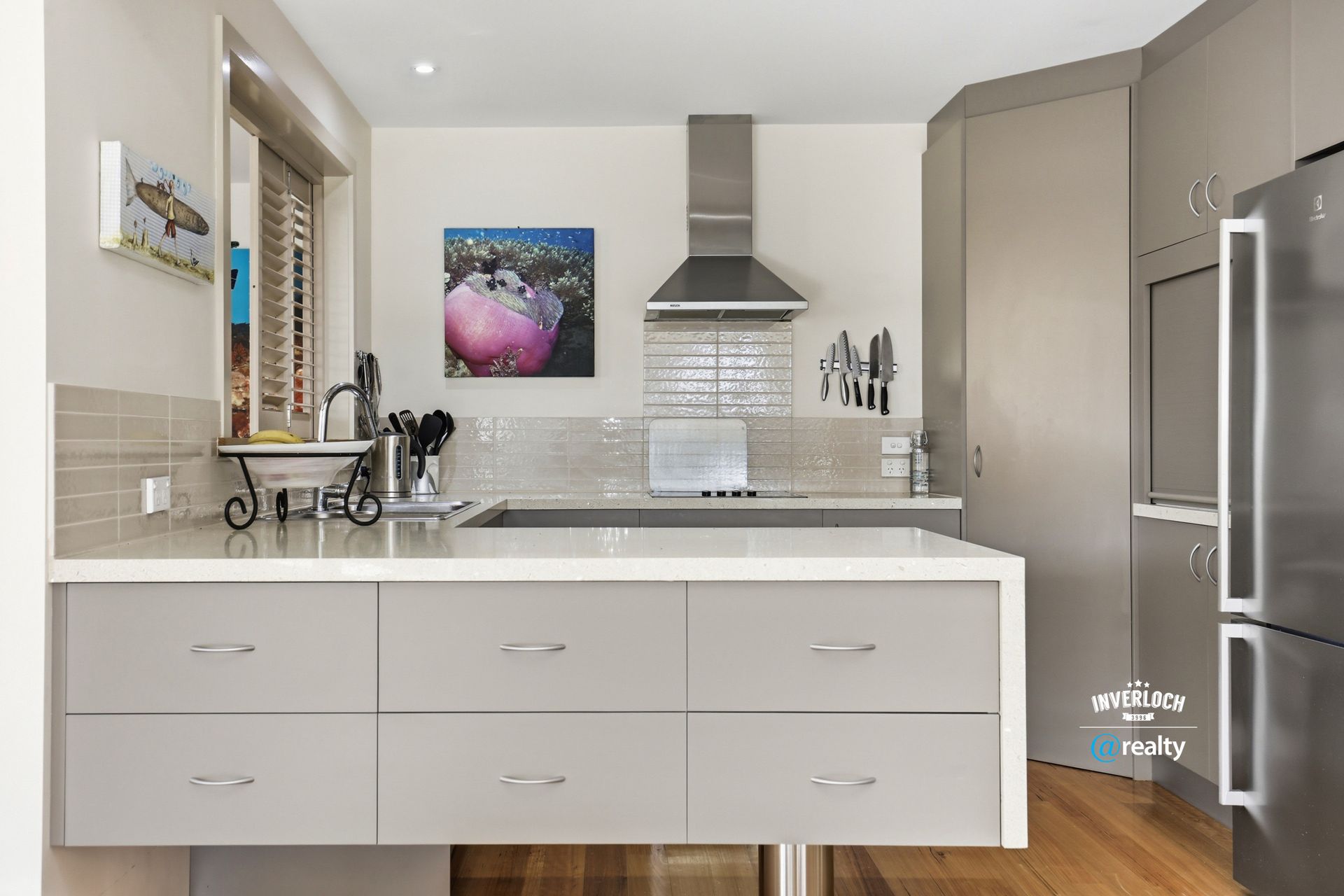 A modern kitchen featuring light gray cabinets, a white island, stainless steel appliances, and a tiled backsplash.