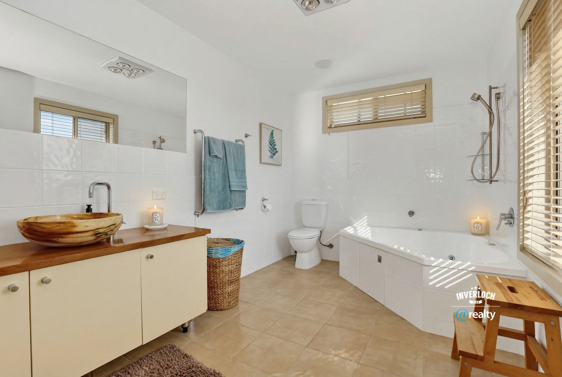 A bright bathroom featuring a wooden vanity, a bowl sink, a corner soaking tub, a toilet, and light-colored tile floors.