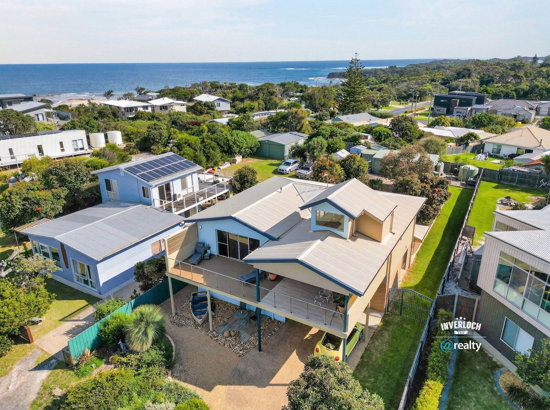Aerial view of modern coastal homes with rooftops, trees, and the ocean in the background.