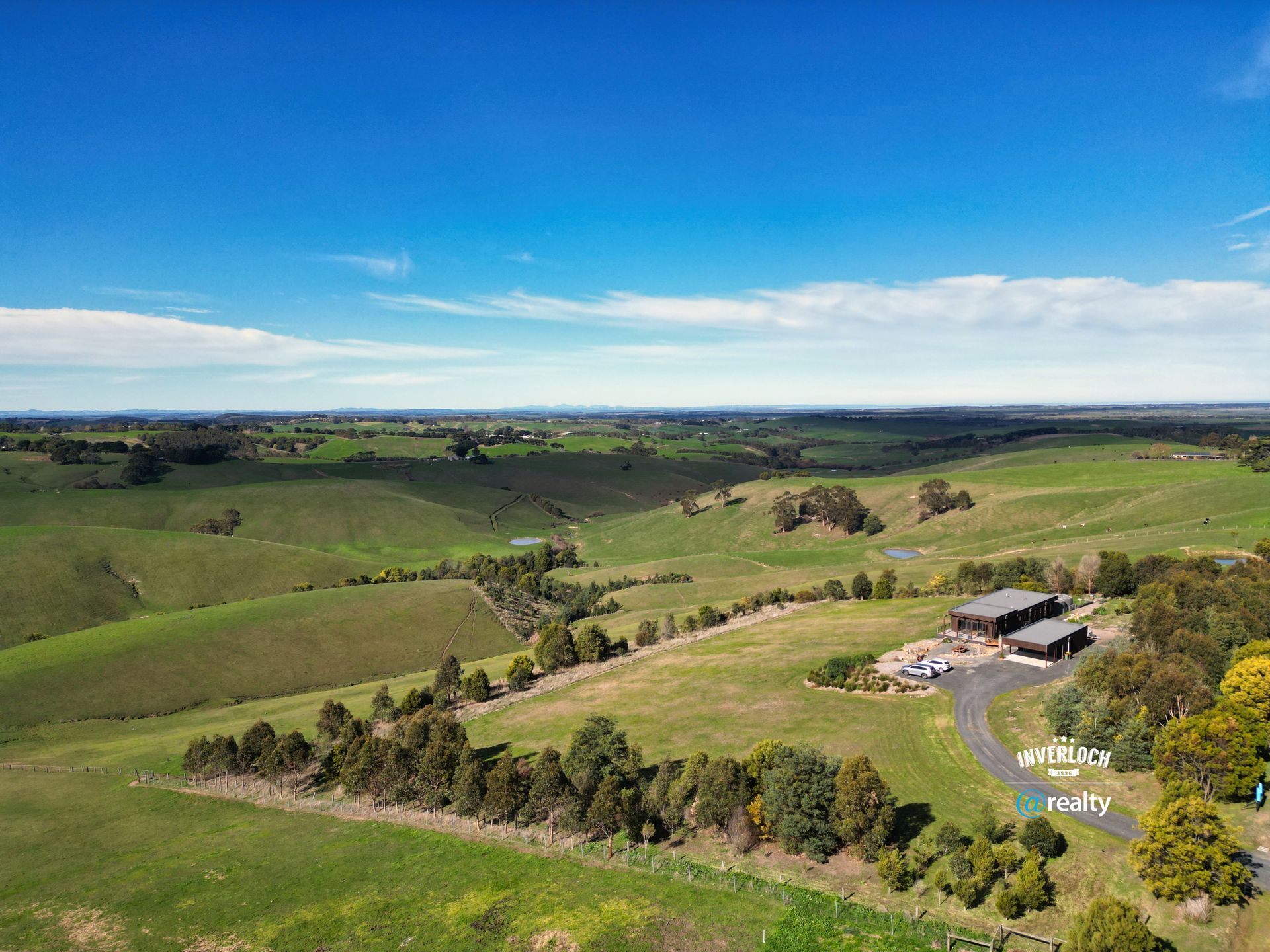Rolling green hills under a bright blue sky. A building and trees are in the foreground.