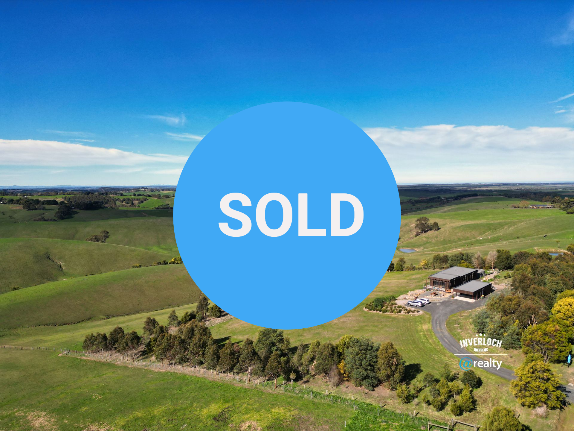 An aerial view of a house in the middle of a field surrounded by trees.