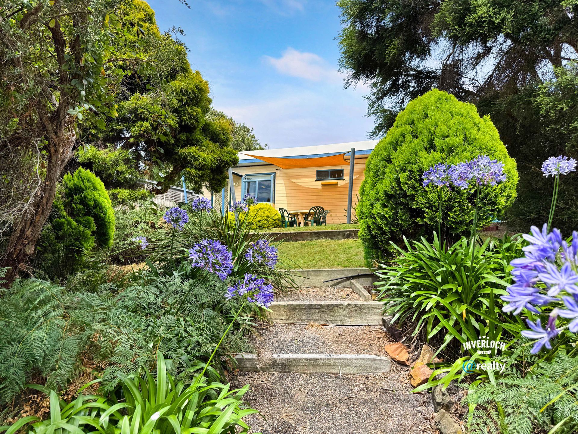 A path leading to a house surrounded by flowers and trees.