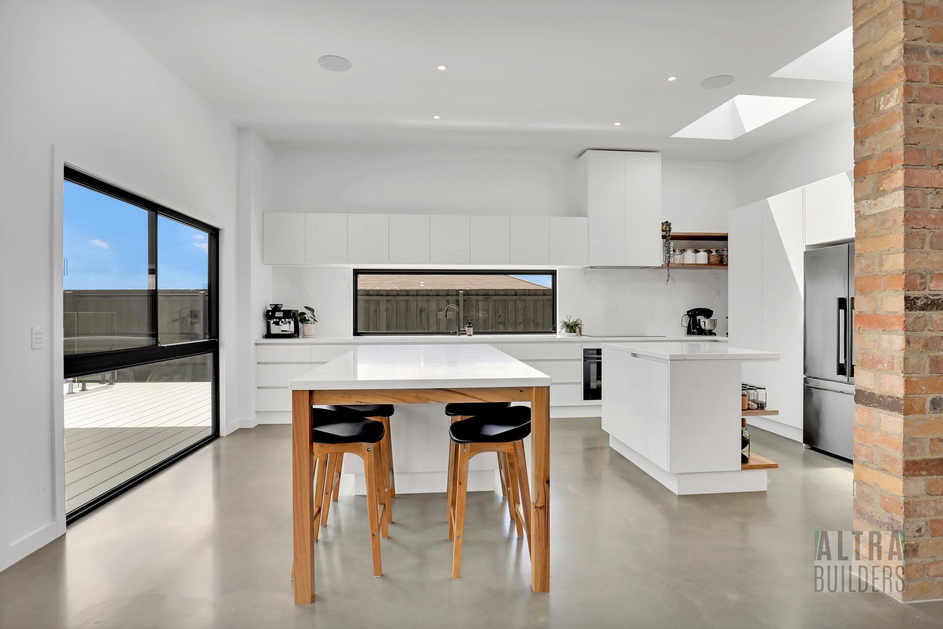 A kitchen with white cabinets , a large island , a table and stools.
