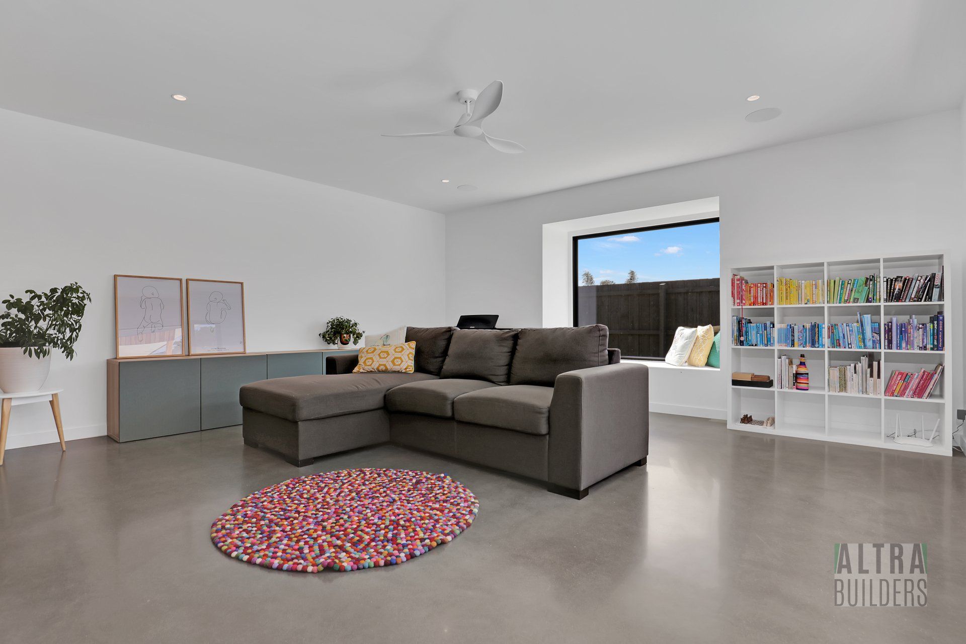 A living room with a couch , rug , bookshelf and window.