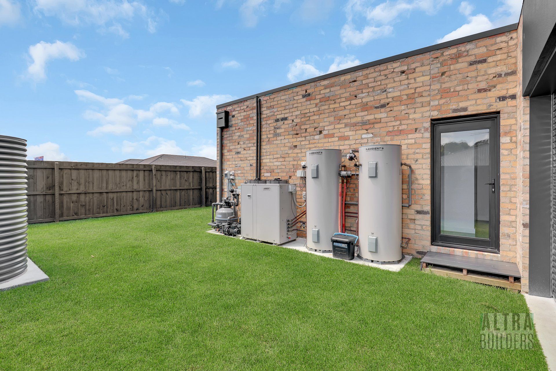 A brick house with two water heaters in the backyard.