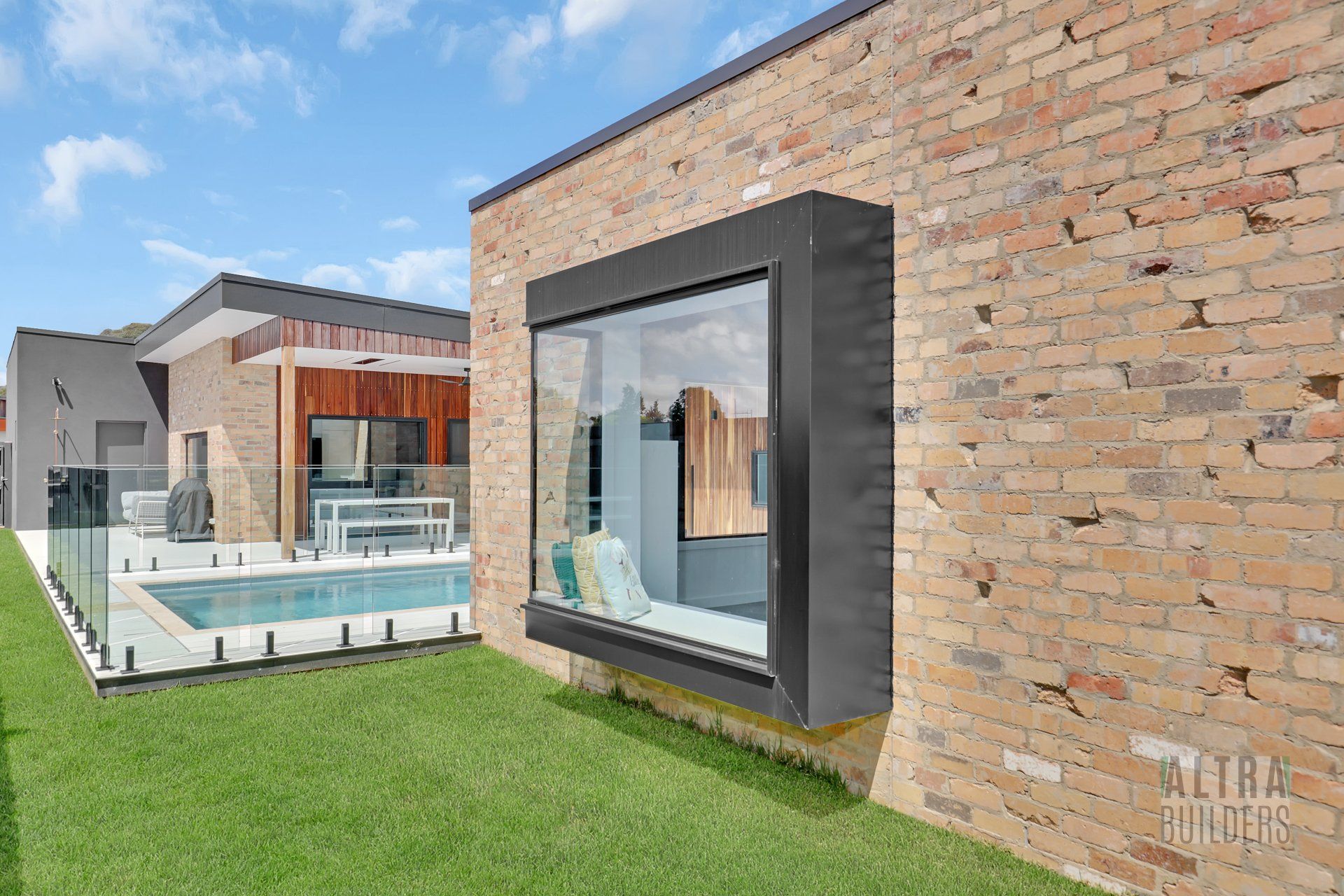 A brick house with a large window and a swimming pool in the backyard.